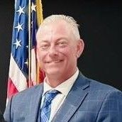 A man in a suit and tie is standing in front of an american flag.