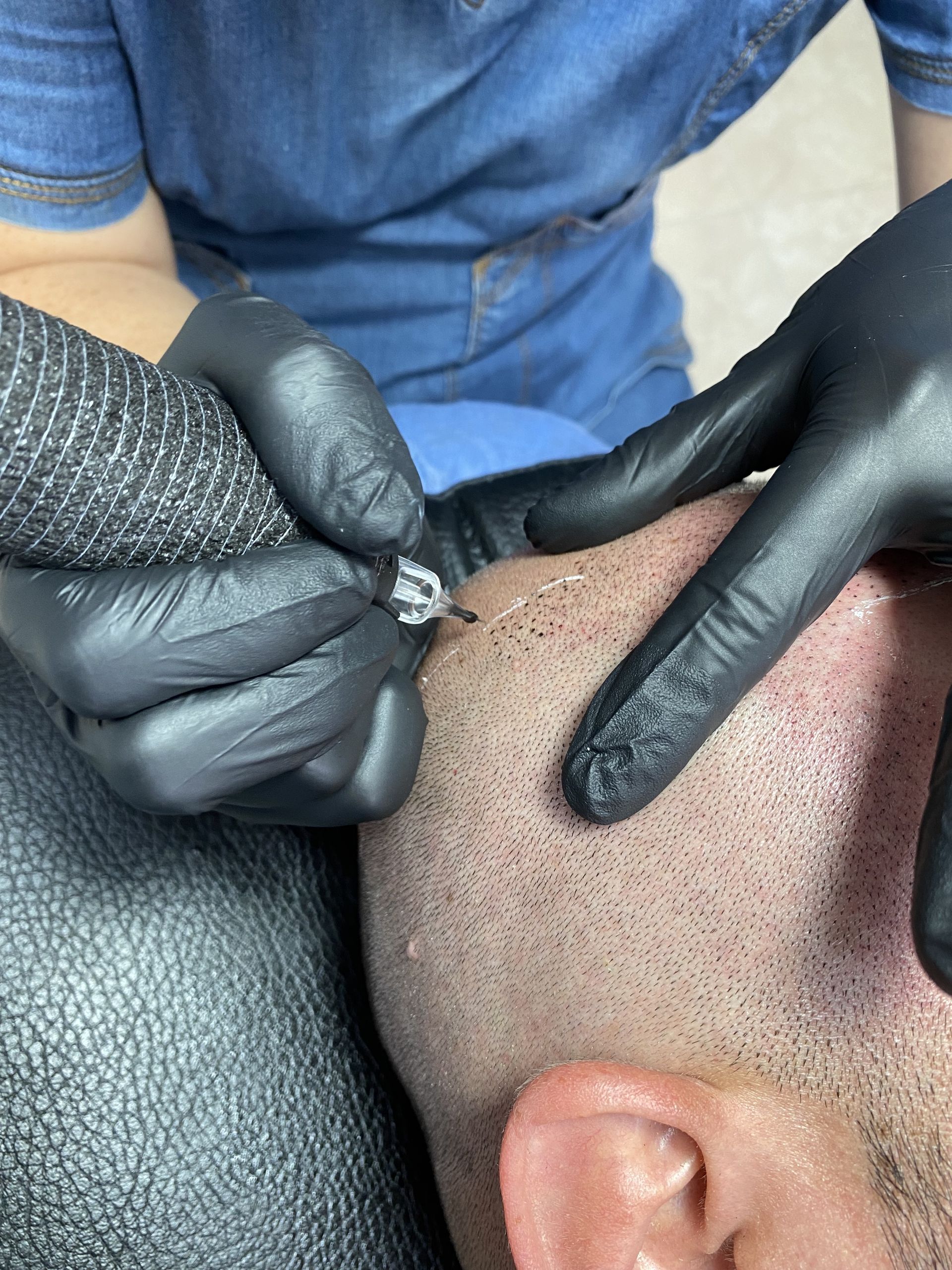 a man is getting a tattoo on his head while wearing black gloves .