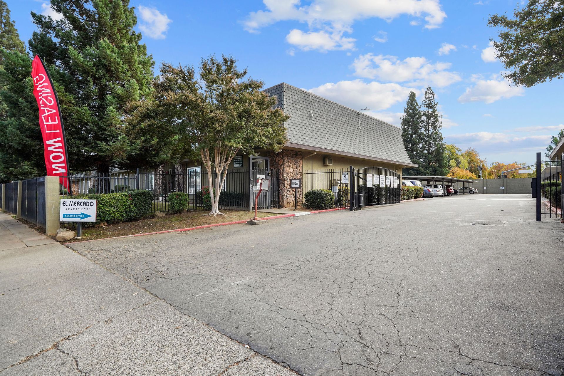 Street view of a rustic building with a red banner, trees, and a wide parking lot under a blue sky
