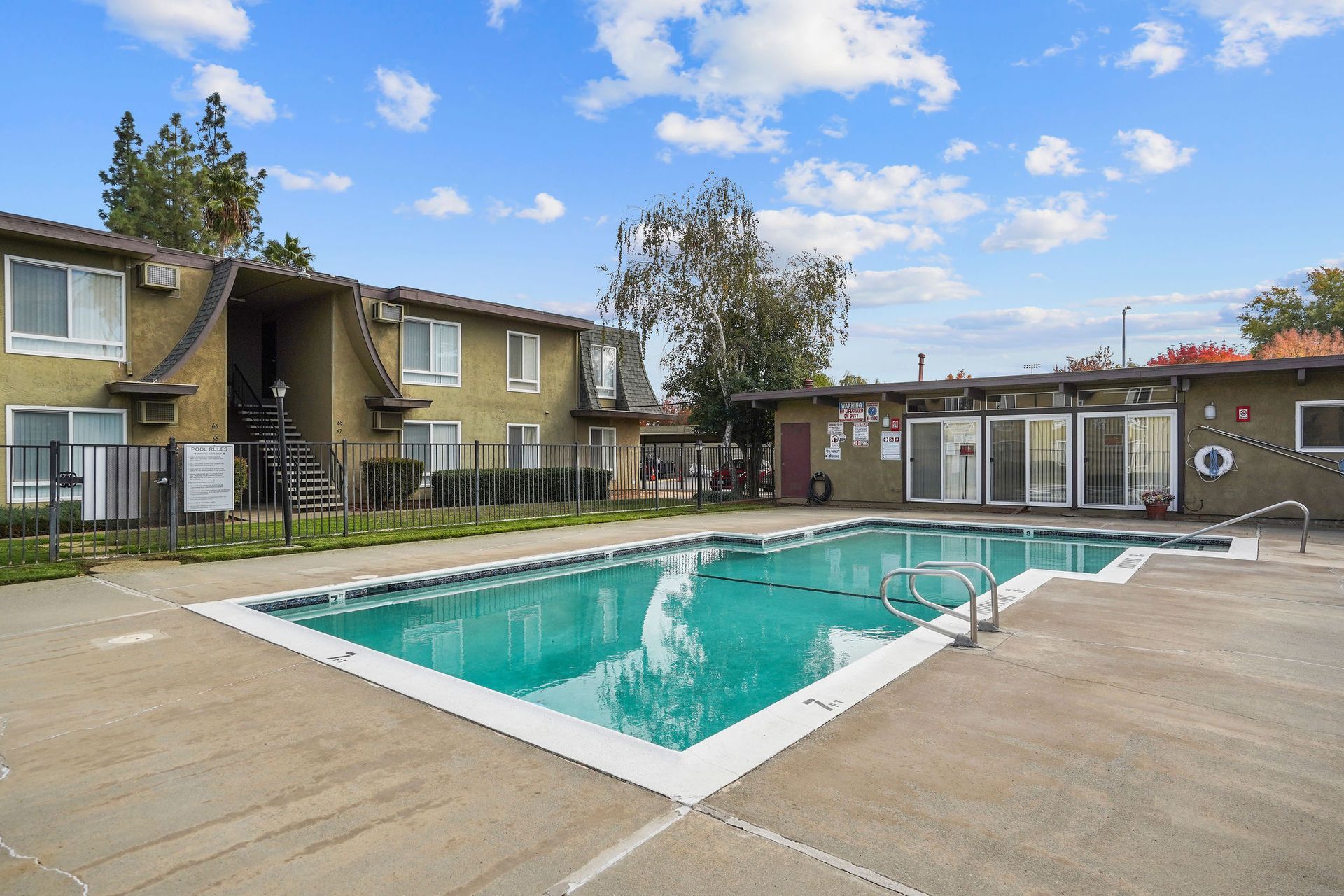 Apartment complex pool with turquoise water and surrounding concrete patio under a blue sky