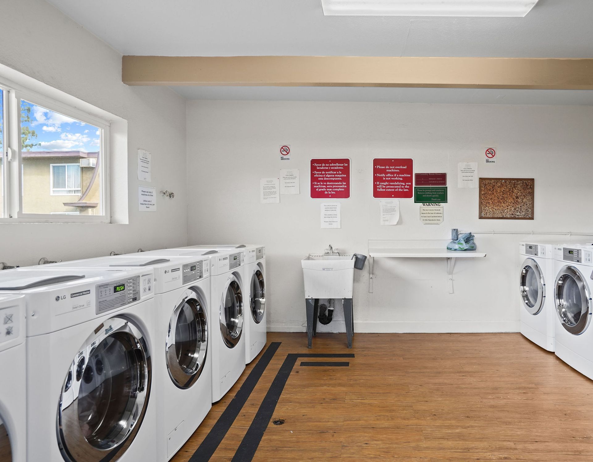 Laundry room with rows of front-load washers and dryers, white walls, and wood-look flooring