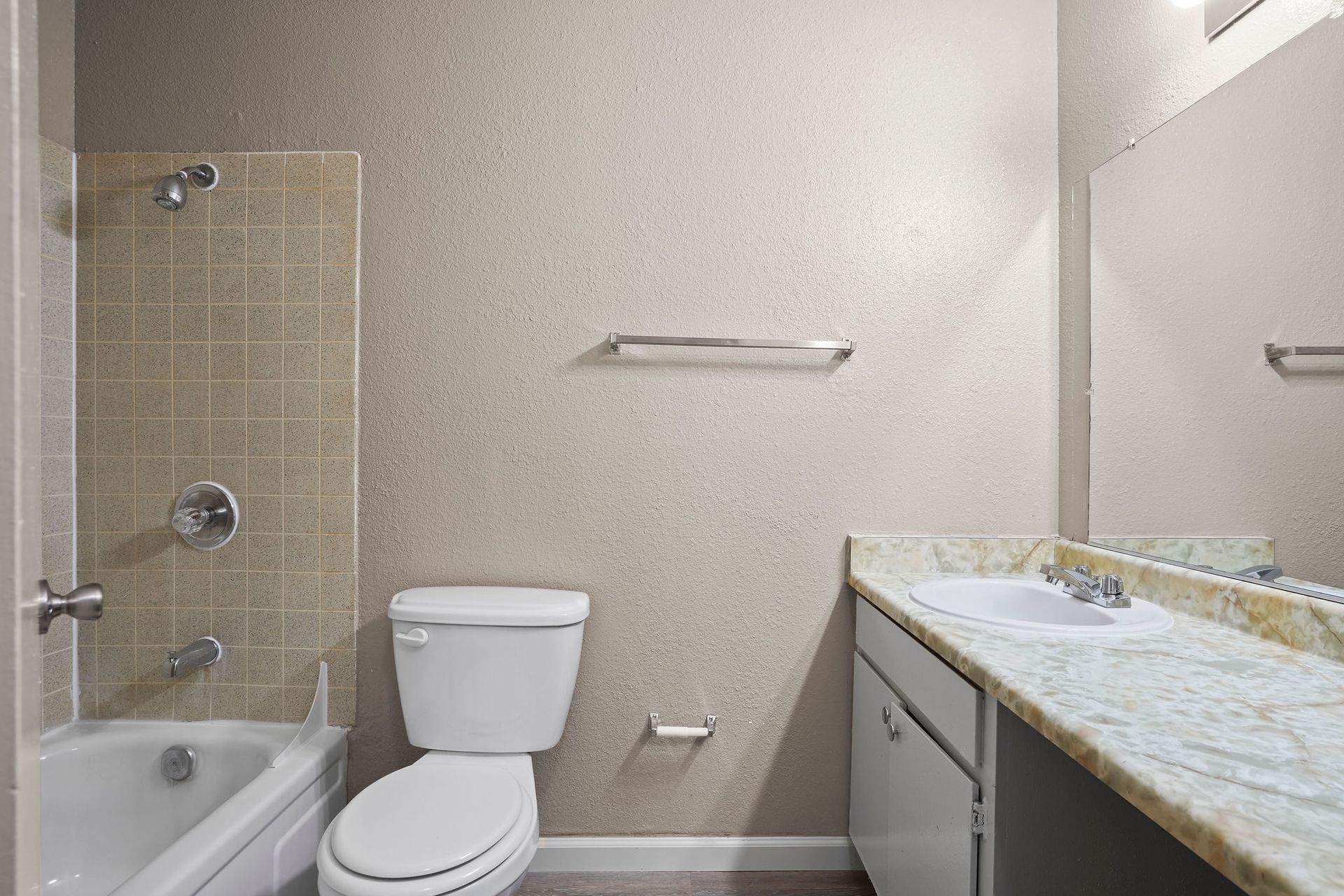 Small bathroom with tub-shower, toilet, towel bar, and vanity with mirror.