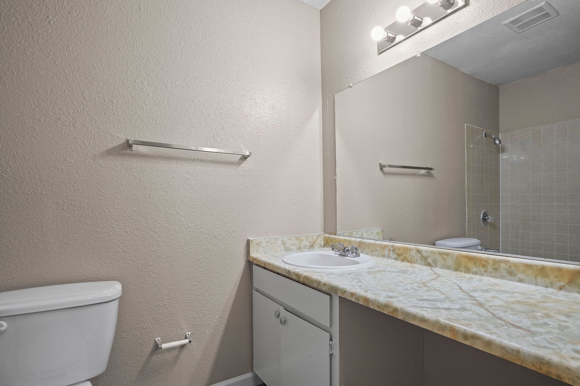 Bathroom with toilet, granite vanity, mirror, and towel bars in beige tones
