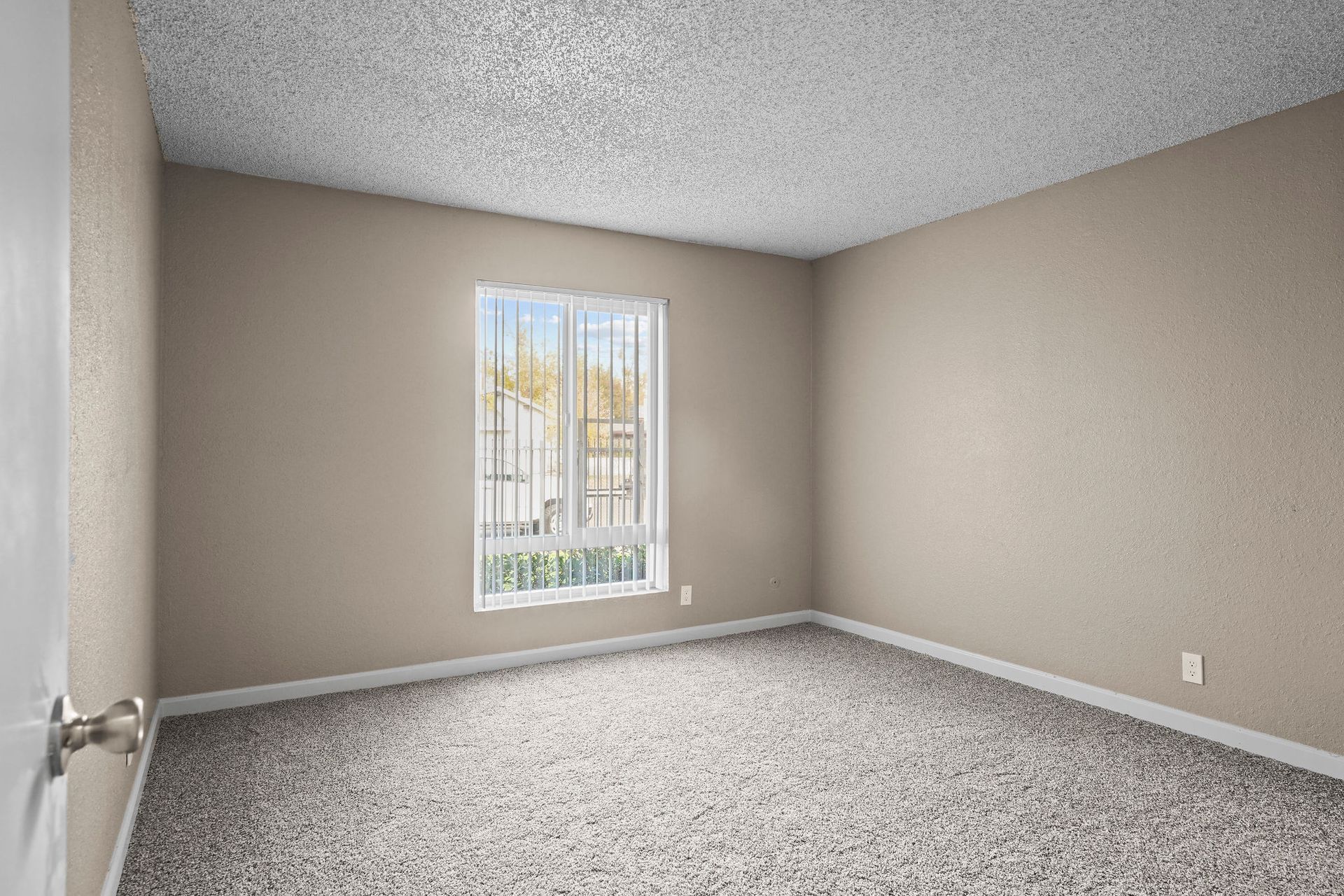 Empty beige bedroom with gray carpet and a window letting in daylight
