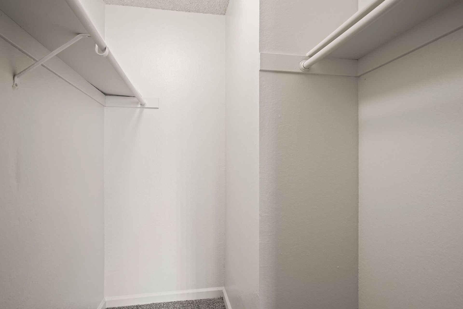 Empty white walk-in closet with hanging rods and shelving on both sides.