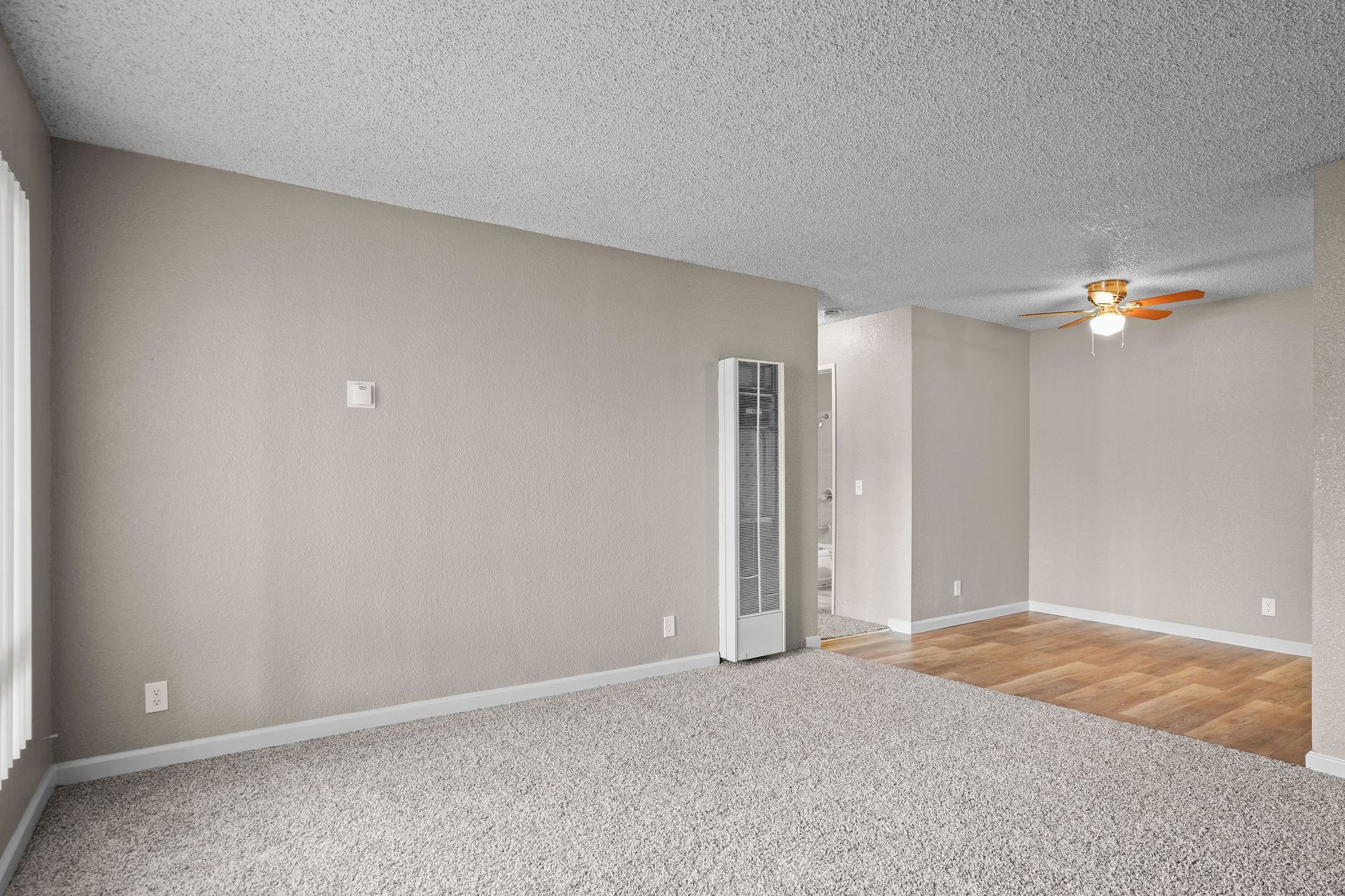 Empty beige living room with carpet, wood floor, and ceiling fan near a doorway