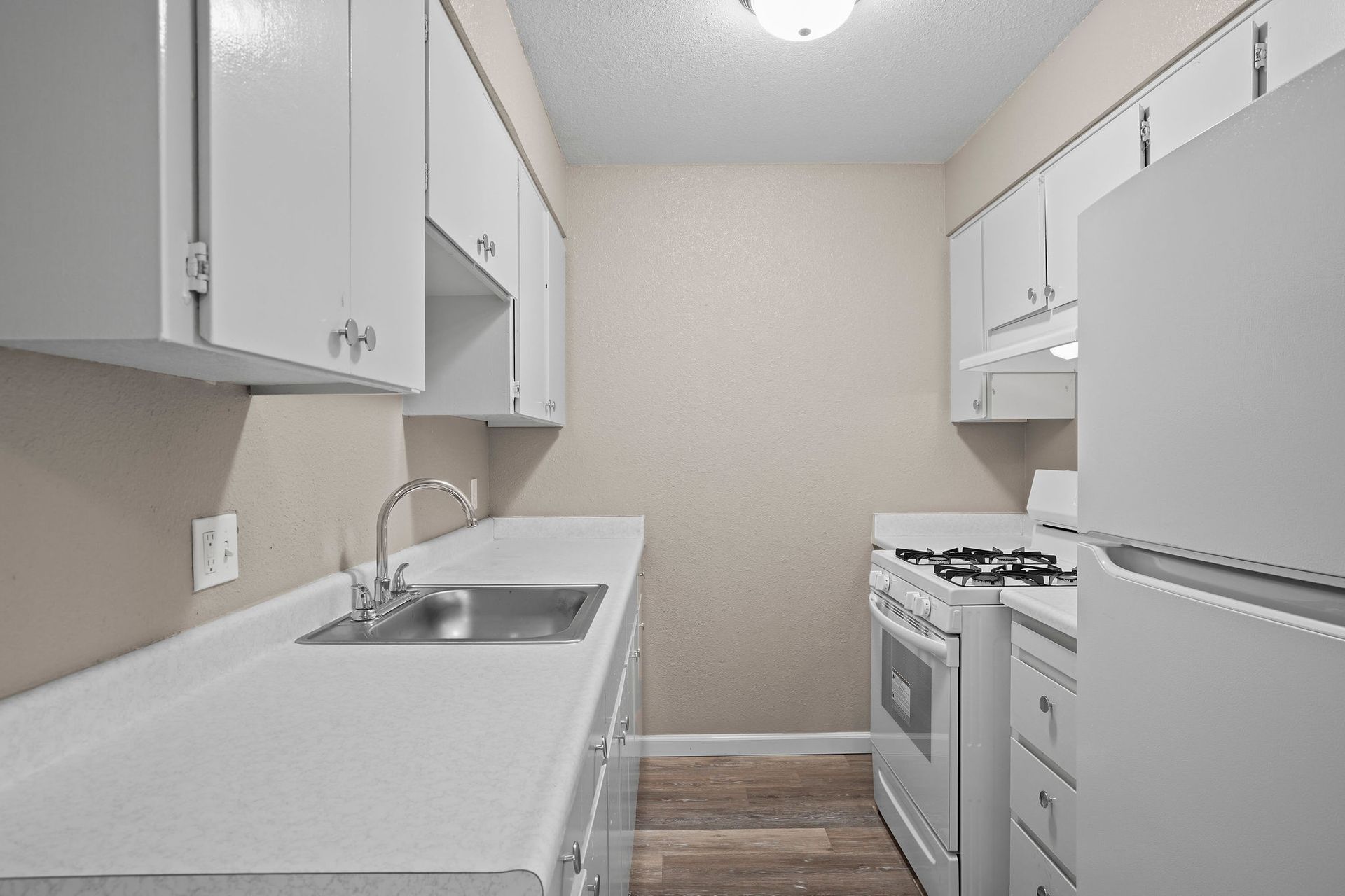Narrow white galley kitchen with gray cabinets, stove, sink, and refrigerator
