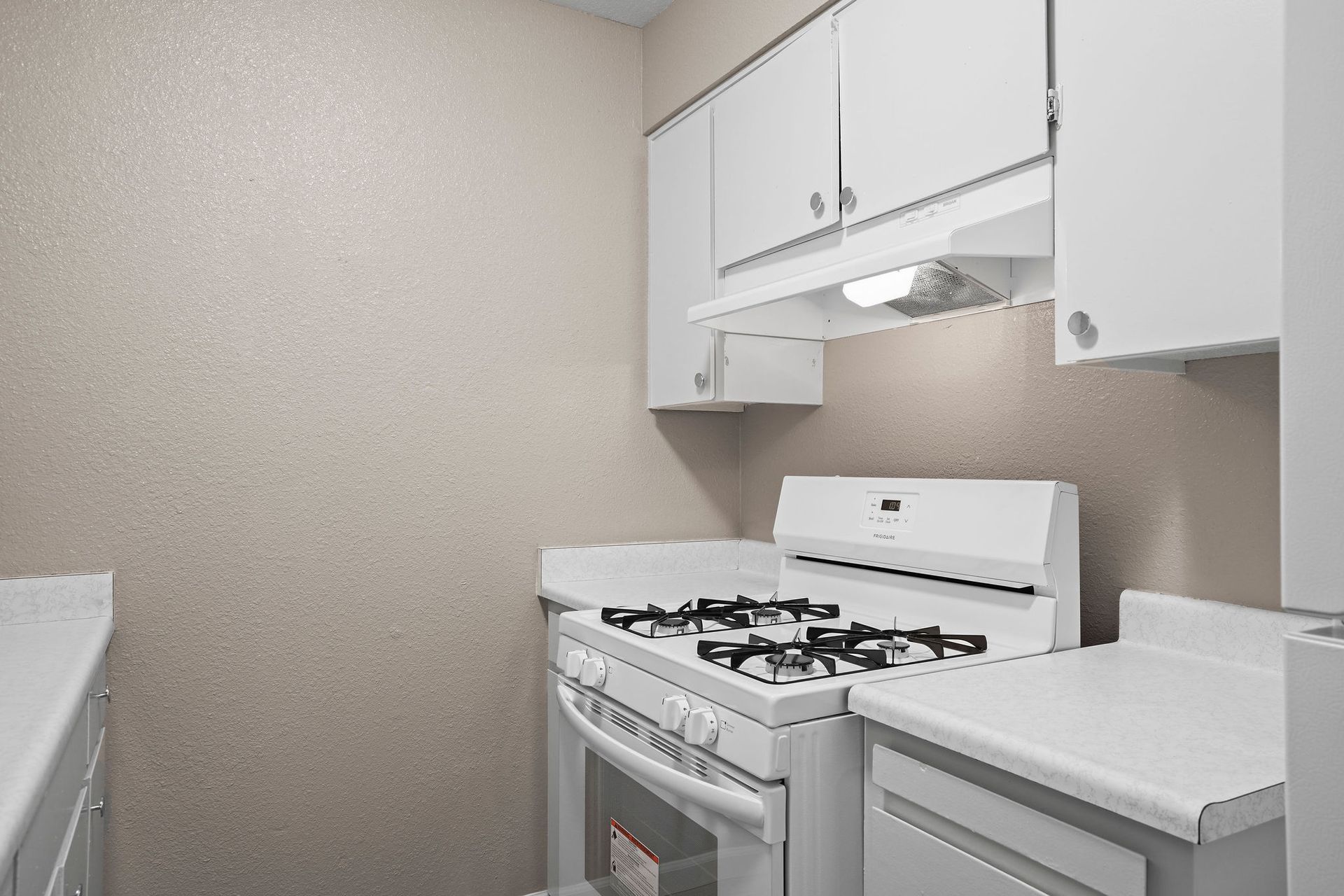 Small white kitchen with gas stove, cabinets, and beige walls.