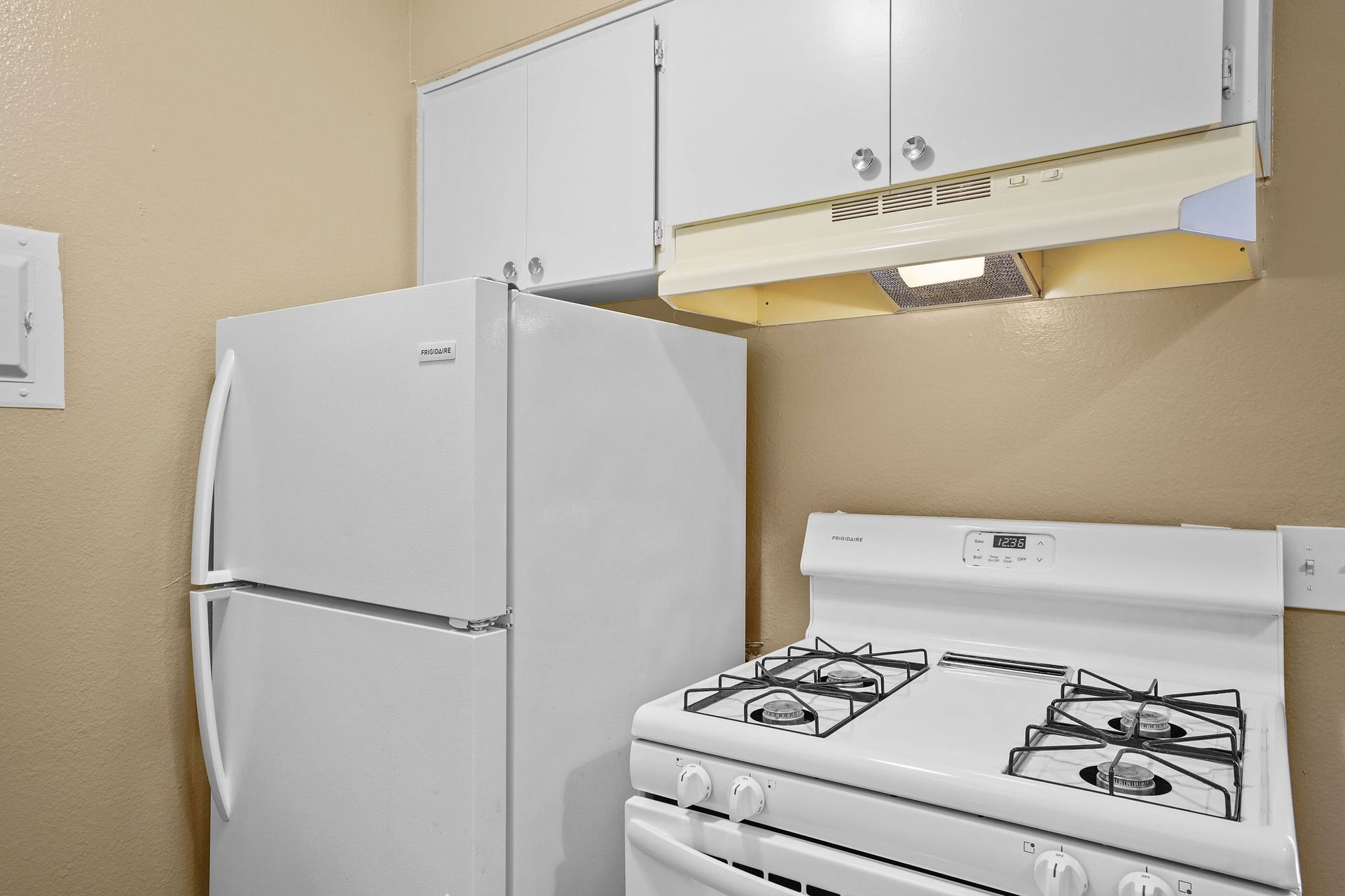 Small kitchen with a white refrigerator, gas stove, and white cabinets under a beige wall.