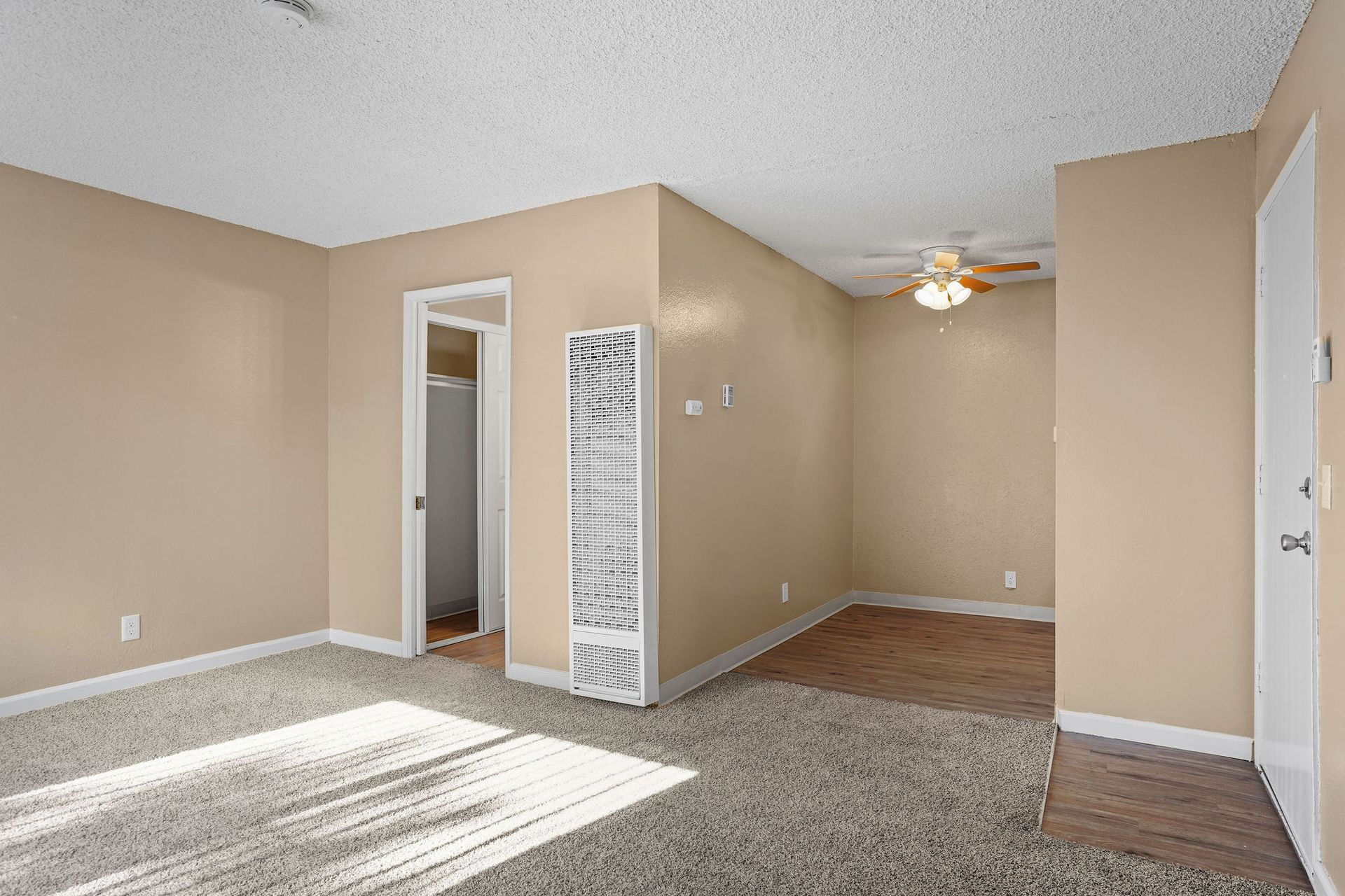 Empty beige living room with carpet, ceiling fan, and doorway to another room.
