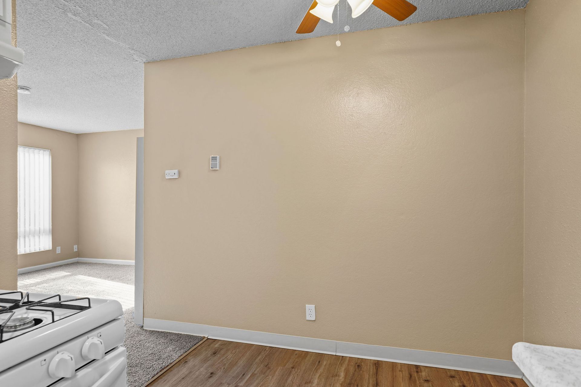 Empty beige wall in a kitchen with hardwood floor and part of a stove visible on the left.