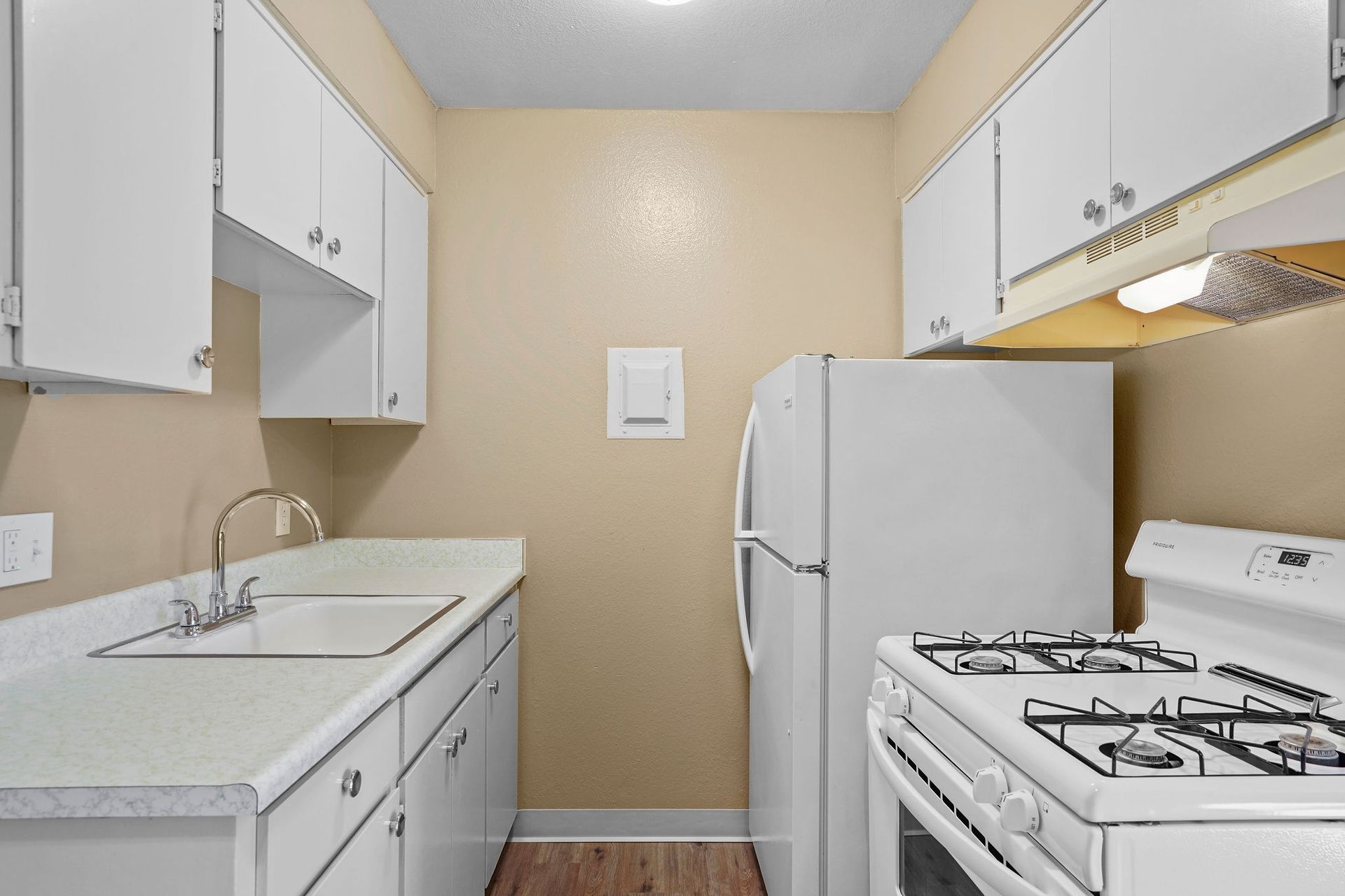 Small white galley kitchen with cabinets, sink, stove, and refrigerator on beige walls