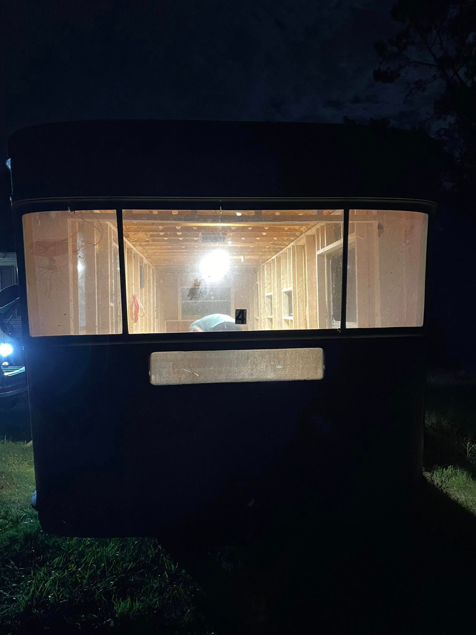 A dimly lit trailer at night, illuminated from within, showcasing an unfinished wooden interior frame.