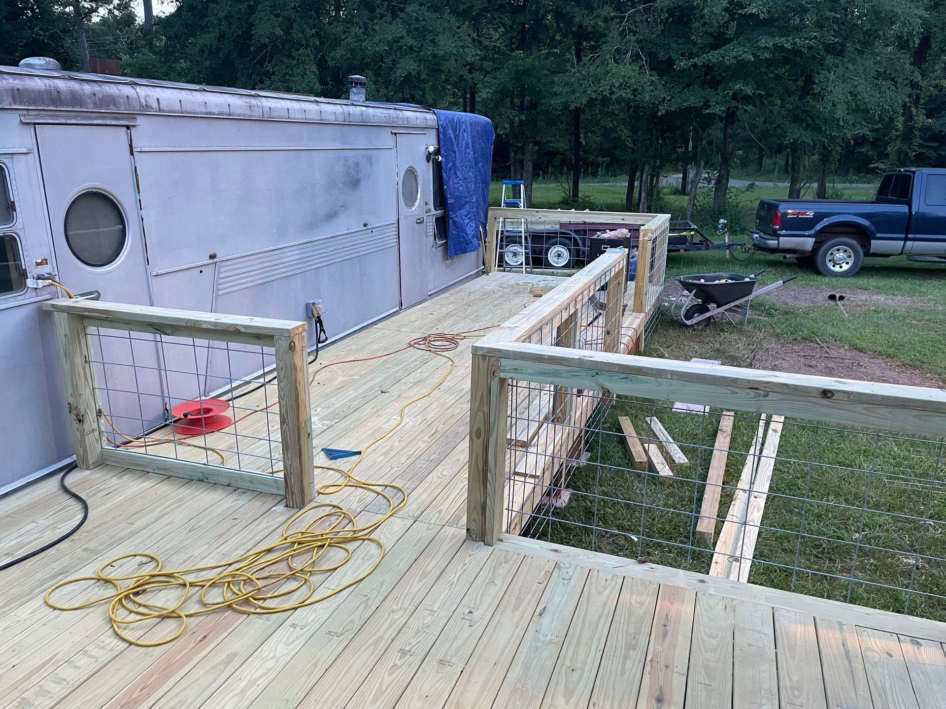 A wooden deck under construction next to a camper, with railings partially installed and a truck parked in the background.