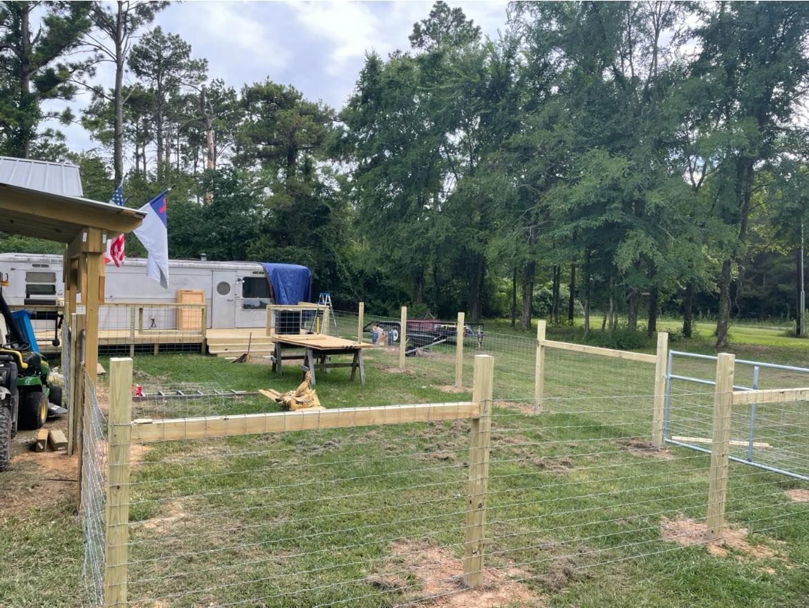 A construction site showing a series of wooden fence posts set in a grassy yard near a house and trees.