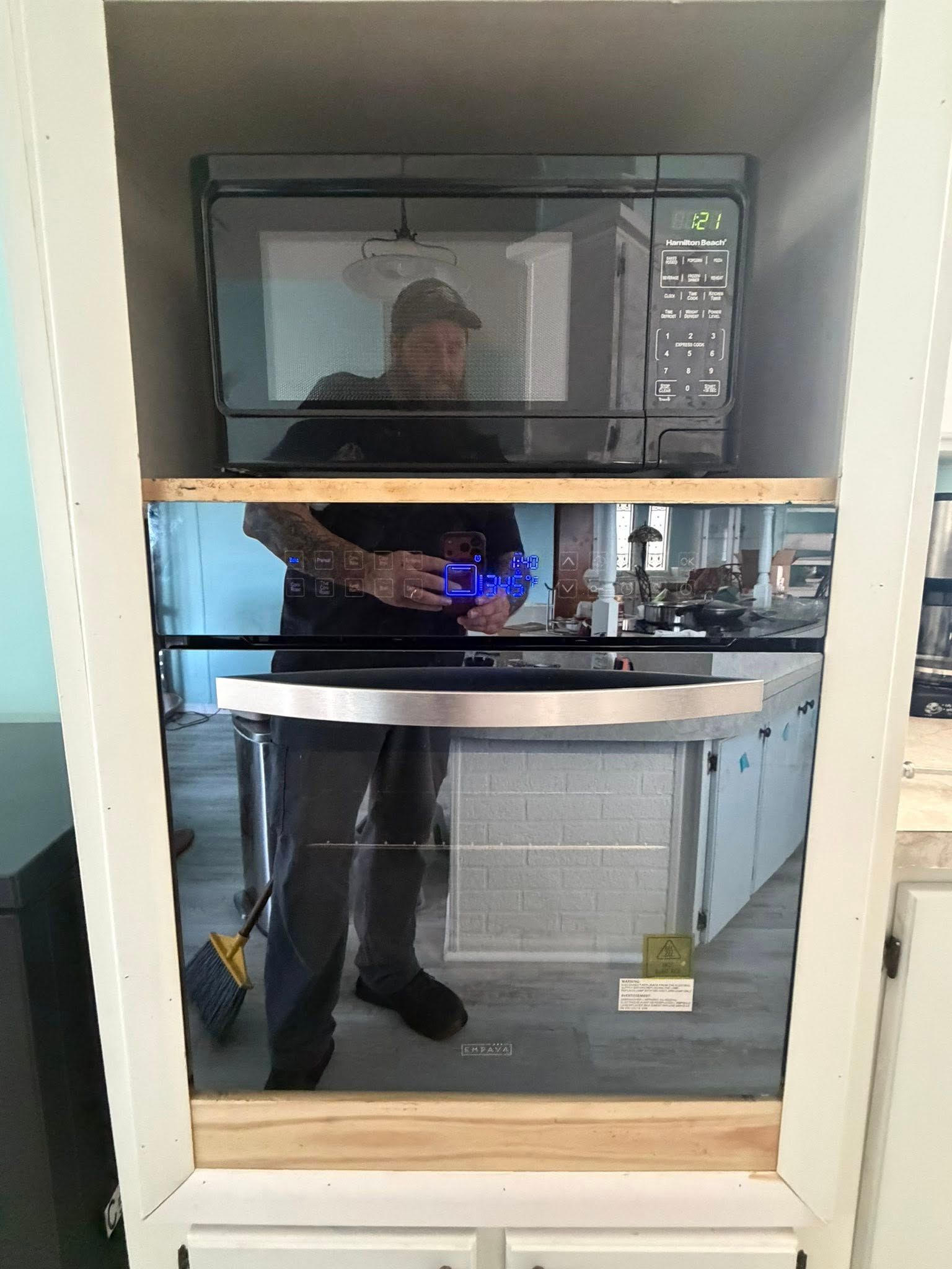 Built-in microwave and toaster oven in a cabinet, with a person reflected in the glass door.