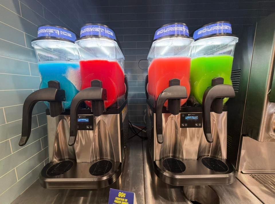 Four frozen drink dispensers in blue, red, orange, and green at a self-serve station