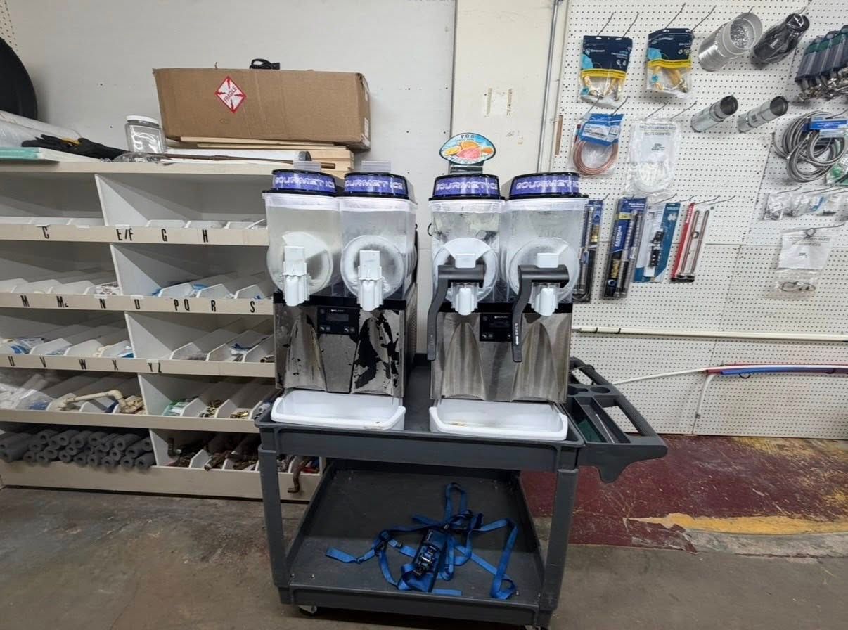 Store display with two countertop beverage dispensers and a row of plastic cups on shelves behind them.