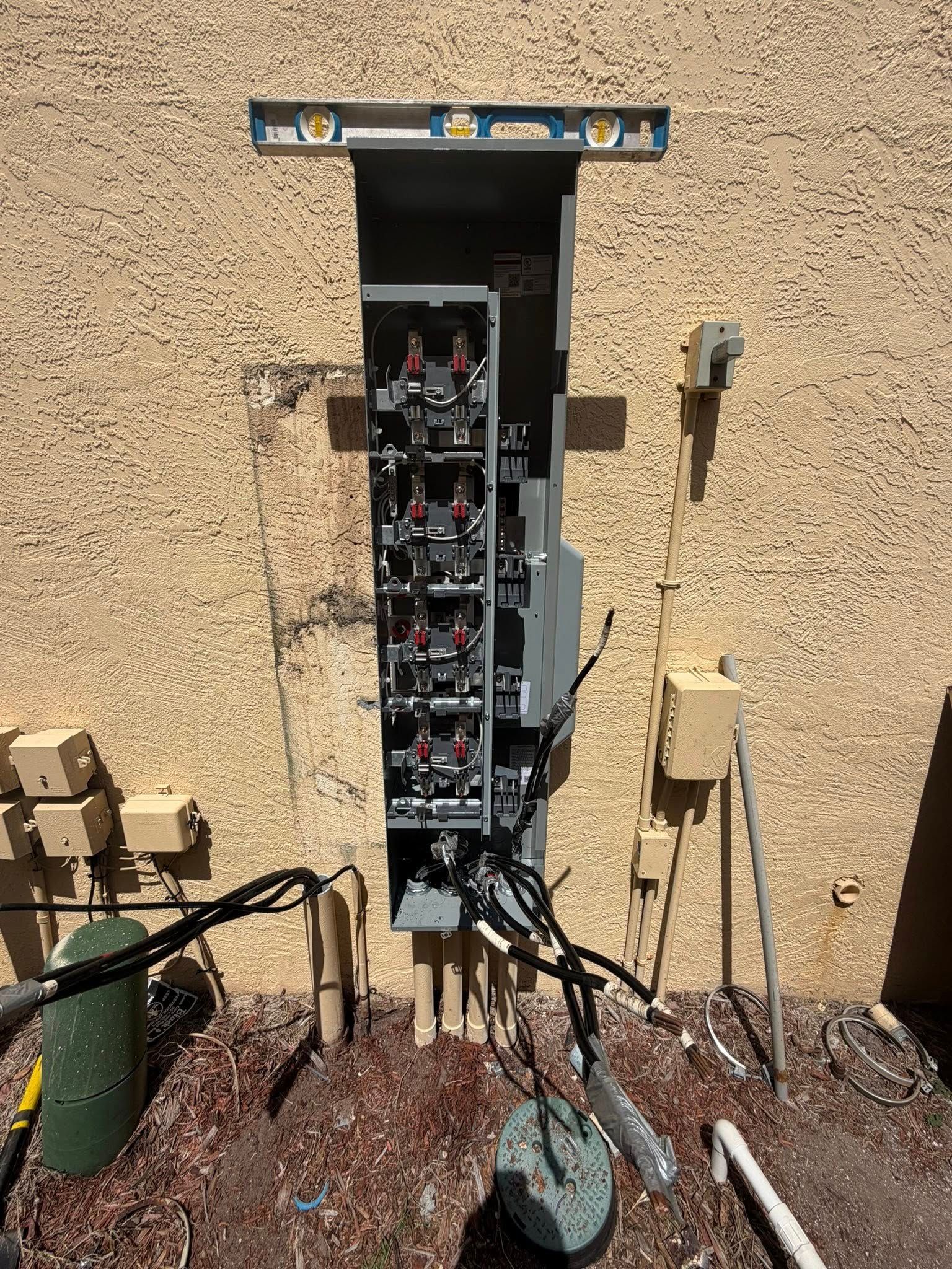 Open electrical panel on stucco wall with exposed wires and meters outdoors.