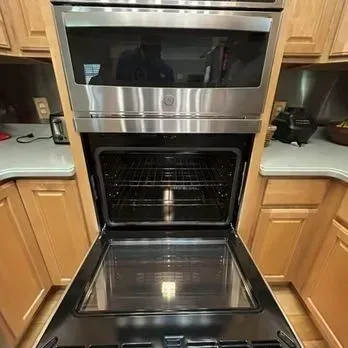 Open wall oven with stainless steel door in a kitchen, showing the interior and lower oven rack.