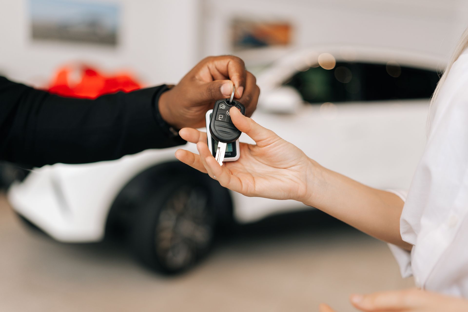 A man is handing a car key to a woman in front of a white car.