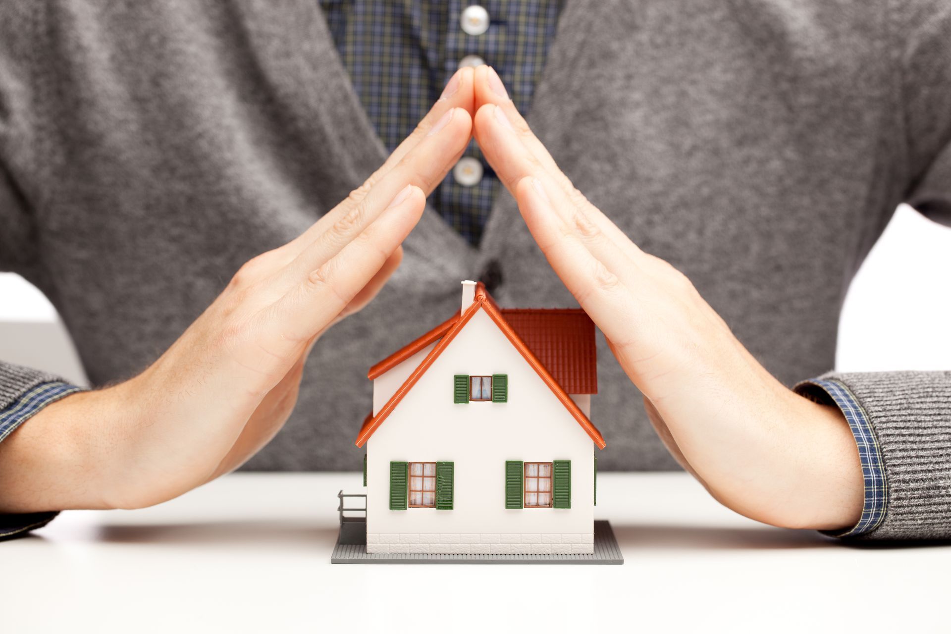 A man is covering a model house with his hands