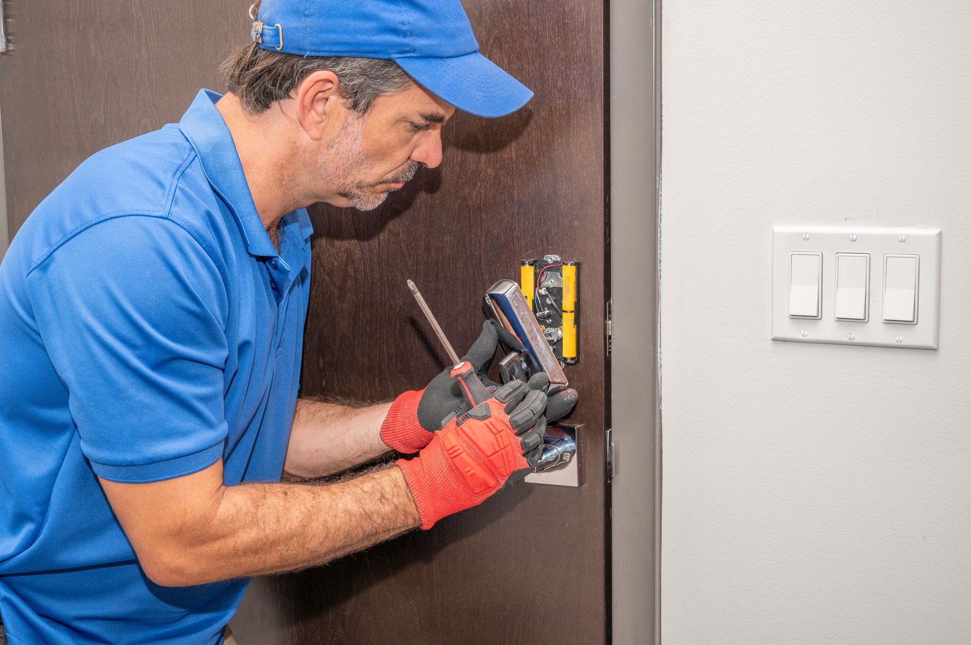 A man in a blue shirt and hat is fixing a door lock.