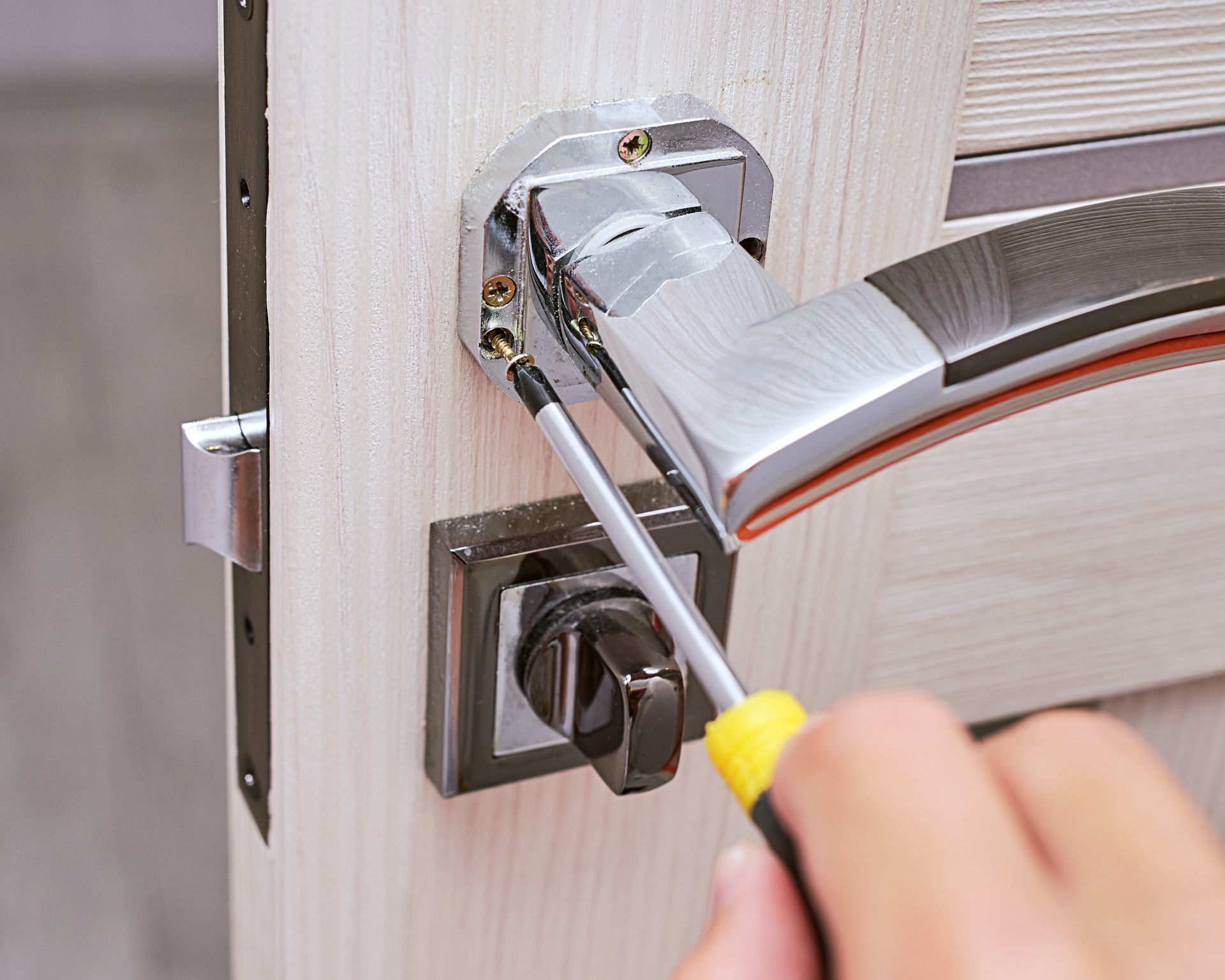 A person is fixing a door handle with a screwdriver.