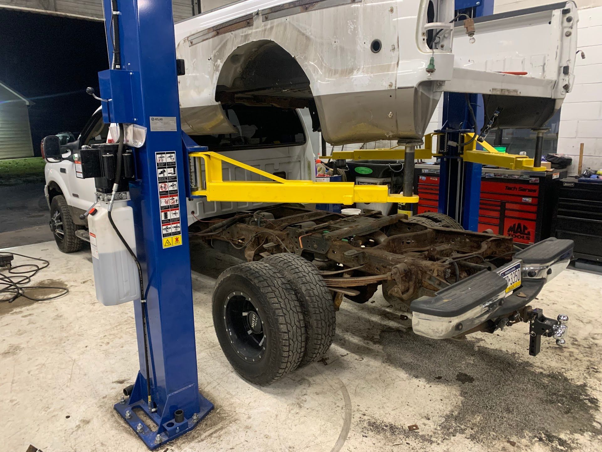 Truck cab being lifted off the frame at a repair shop, revealing chassis. Blue lift, yellow supports | JP Automotive, LLC