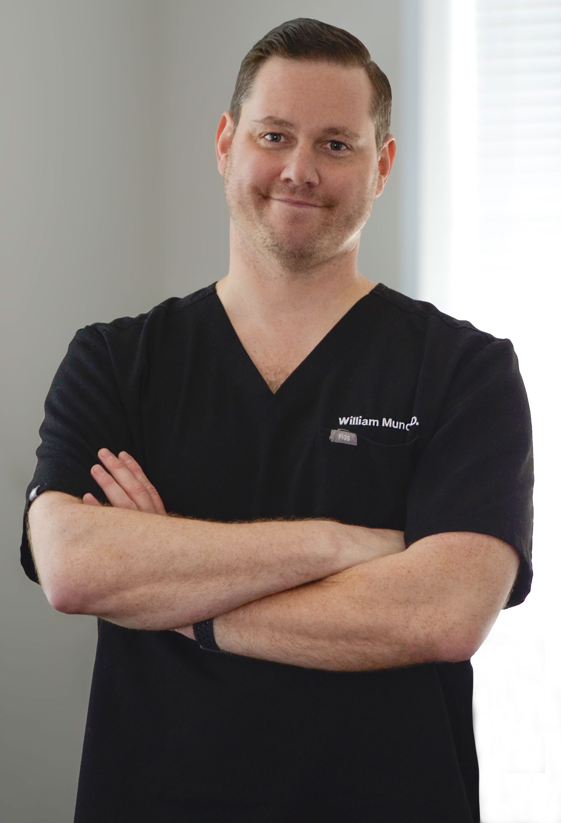A man in a black scrub top with his arms crossed