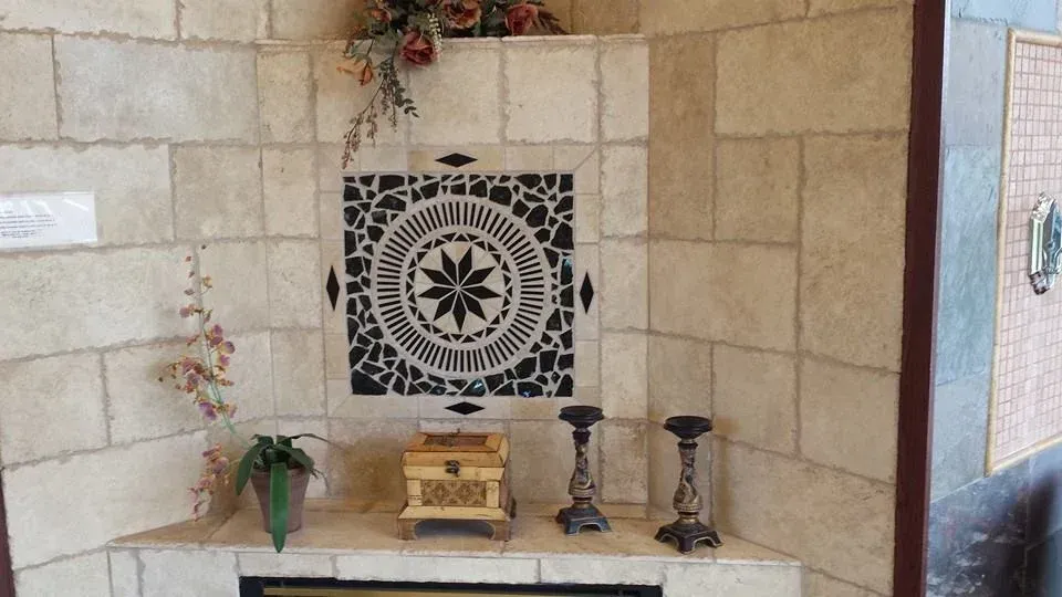 A decorative corner fireplace with light-colored stone tiles. A central mosaic panel displays a black and white 