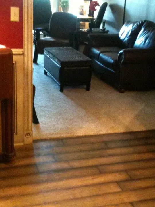 Hardwood floor transitions to carpeted living room with black leather furniture.