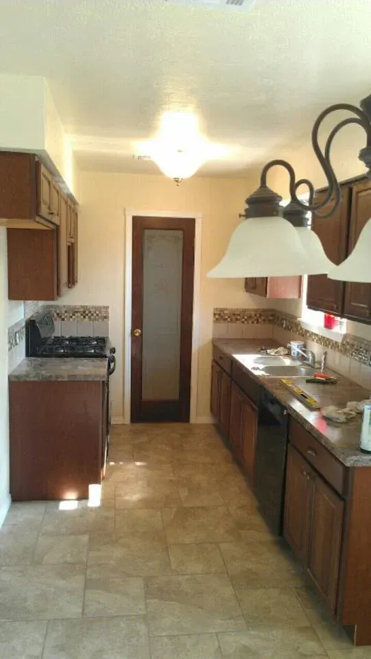 Kitchen with brown cabinets, tile backsplash, and a frosted glass door at the end. Beige walls and tile floor.