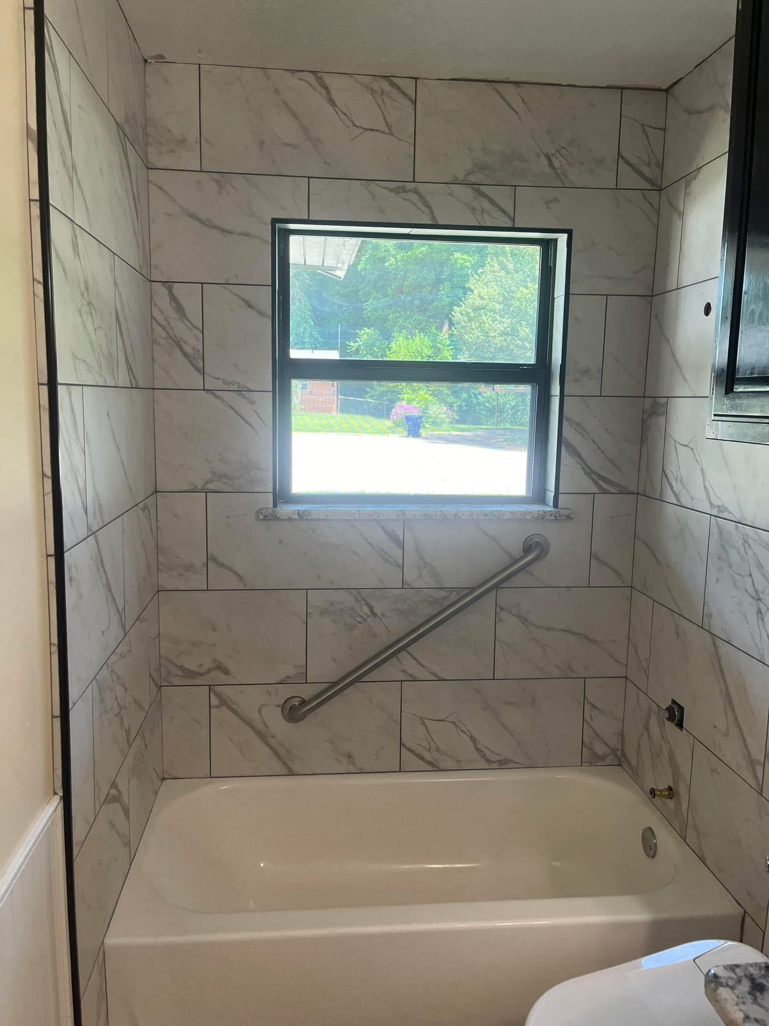 Bathroom with white and gray marble-look tiled walls, a bathtub, window, and a silver grab bar.