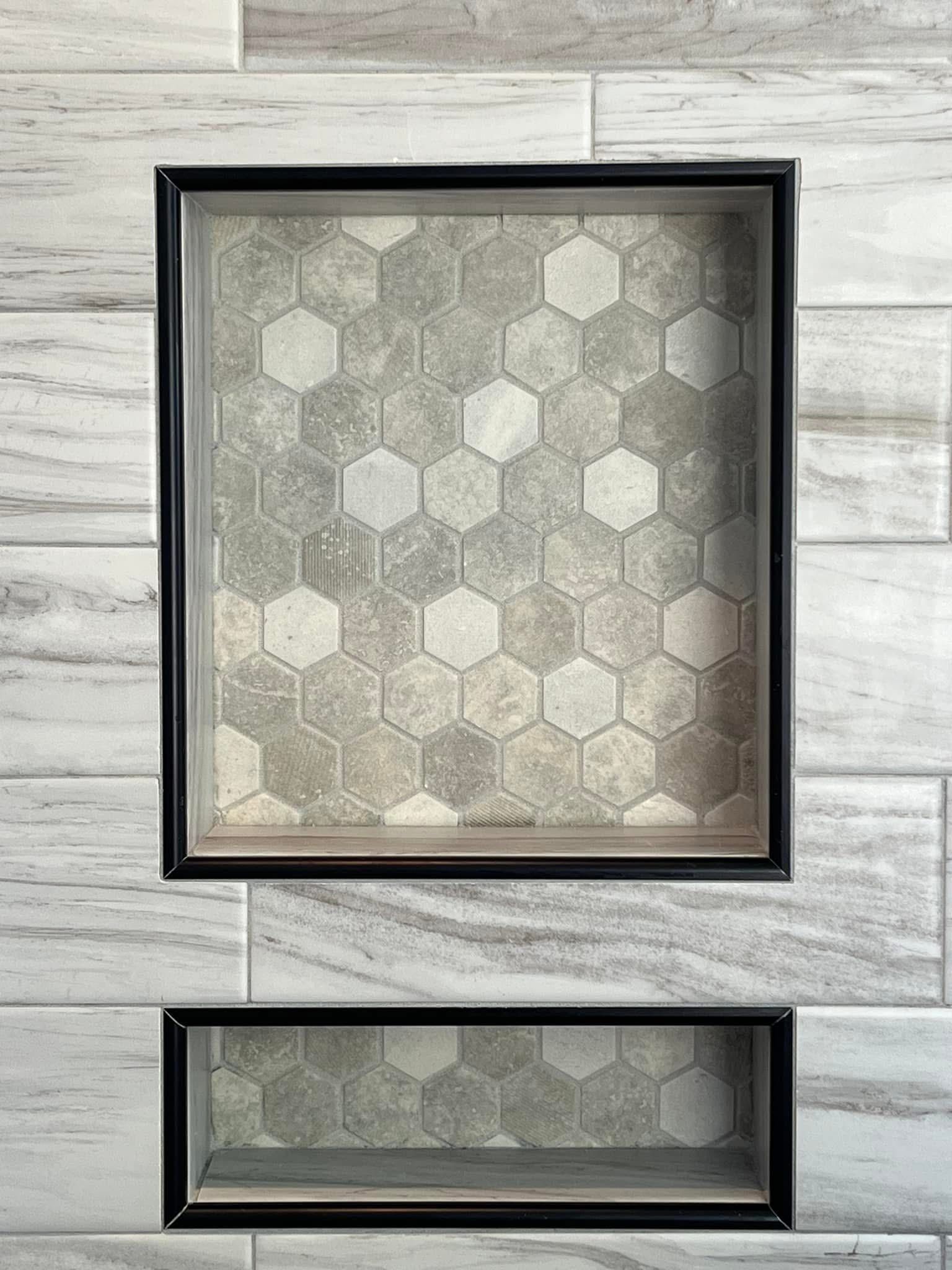 Two recessed shower niches framed in black, tiled with gray and white hexagonal tile