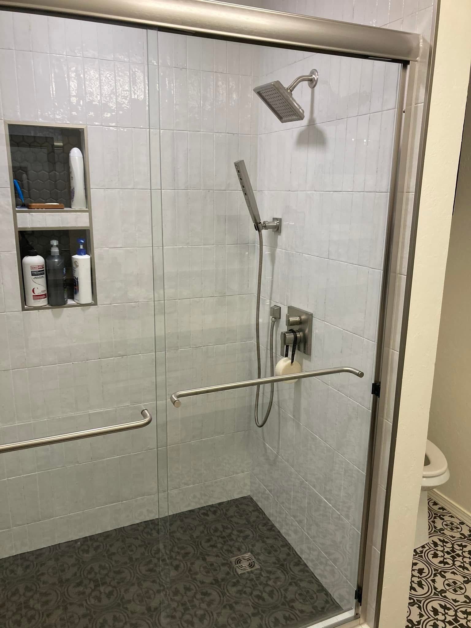 A modern shower with gray and white tile, a glass door, and built-in shelf holding toiletries.