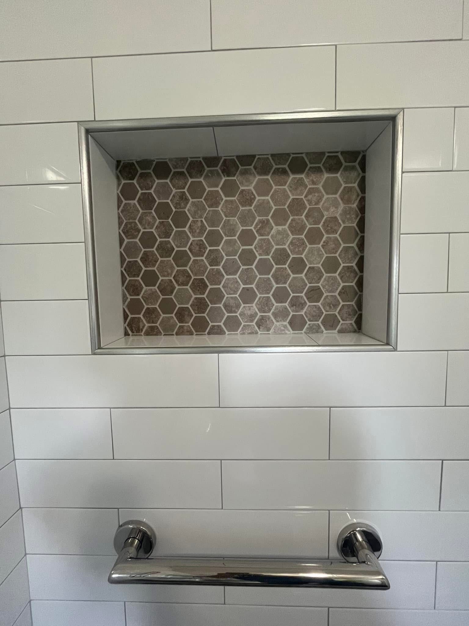 Bathroom niche with silver frame and hexagon tile backing, surrounded by white subway tiles. A silver shelf is below.