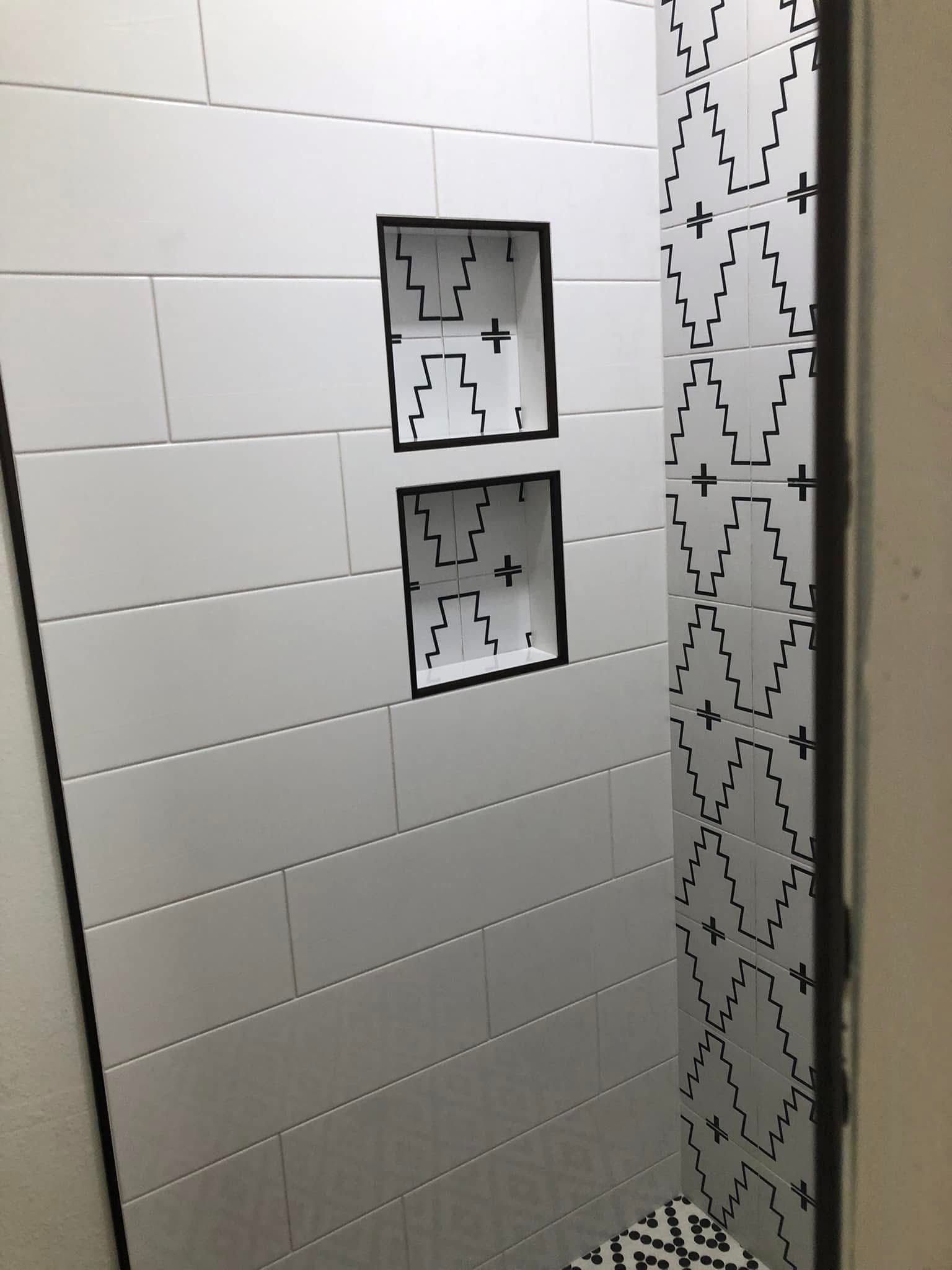 Bathroom shower tiled with white horizontal rectangles and patterned black and white design. Two built-in niches are visible.
