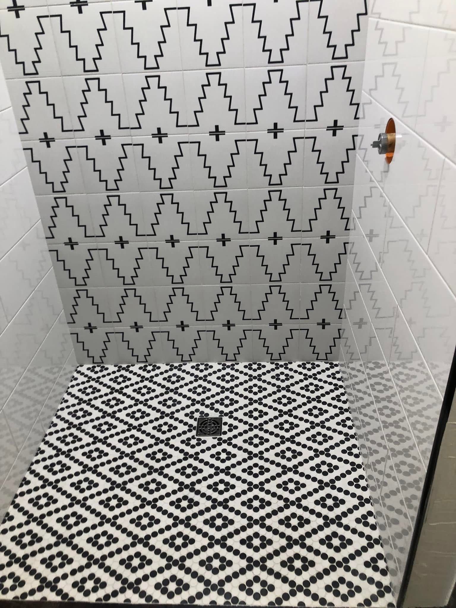 Black and white tiled shower with geometric patterns on the floor and upper walls. A shower head is visible.