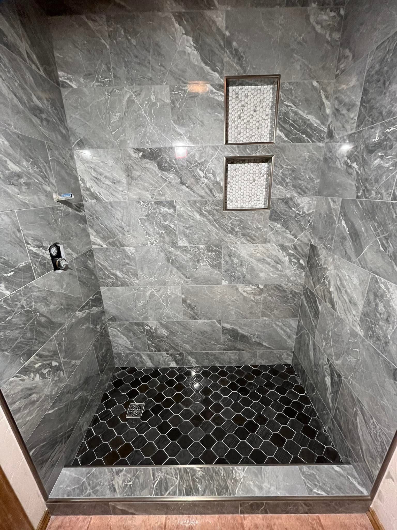 Gray-tiled shower with black patterned floor and two built-in shelves. The shower features a dark gray marble-like pattern.