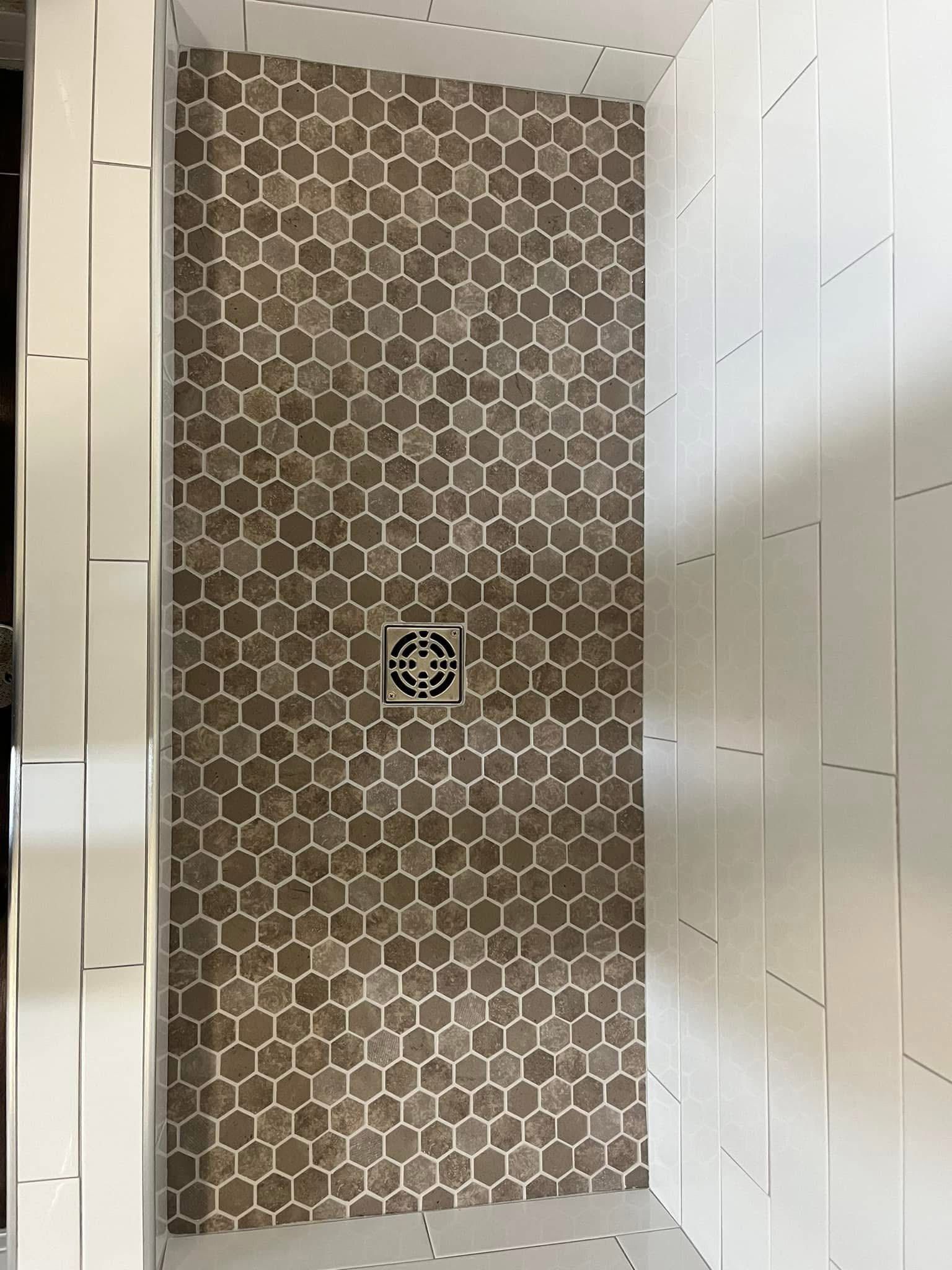 Shower stall with brown honeycomb tile floor and white rectangular wall tiles. A drain is centered in the floor.