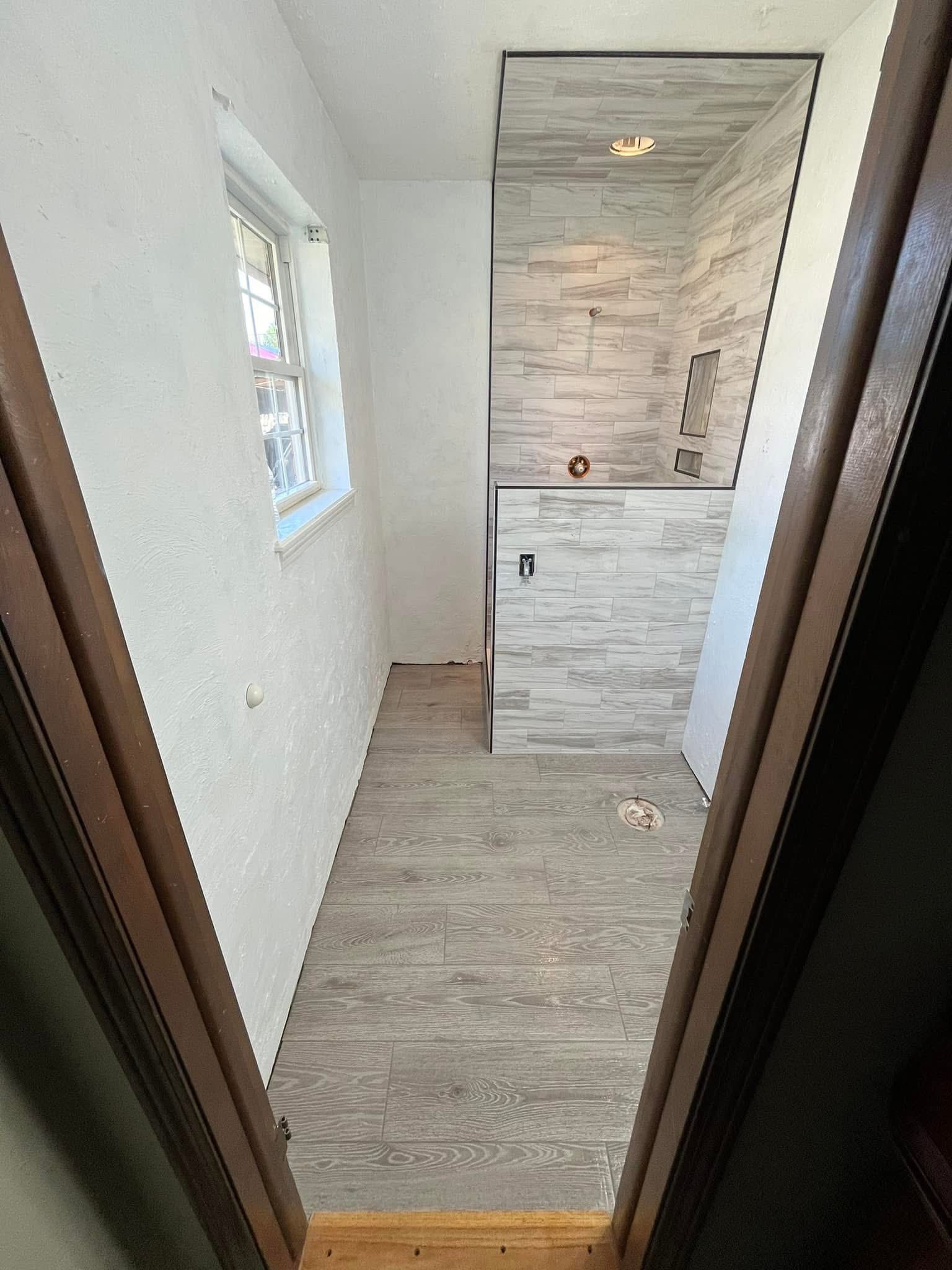 A narrow, recently renovated bathroom with light gray wood-look tile floor and textured wall tile. 