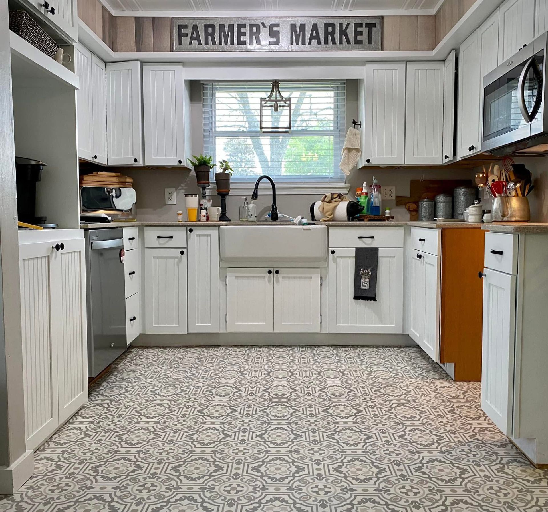 White farmhouse-style kitchen with a gray and white patterned floor and farmer's market sign above the window.