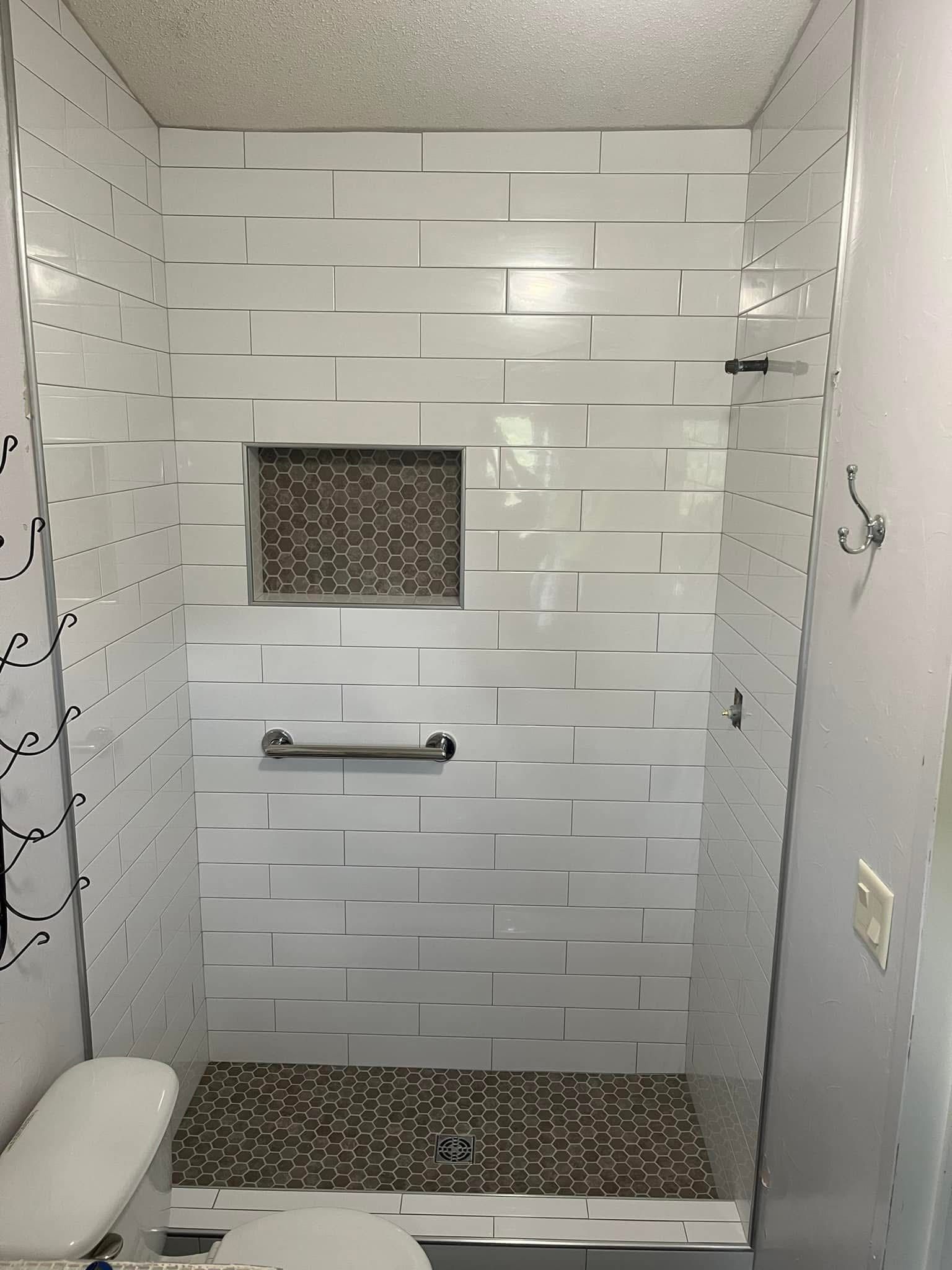 A tiled shower with a dark mosaic floor and a built-in shelf. A grab bar is installed on the shower wall.