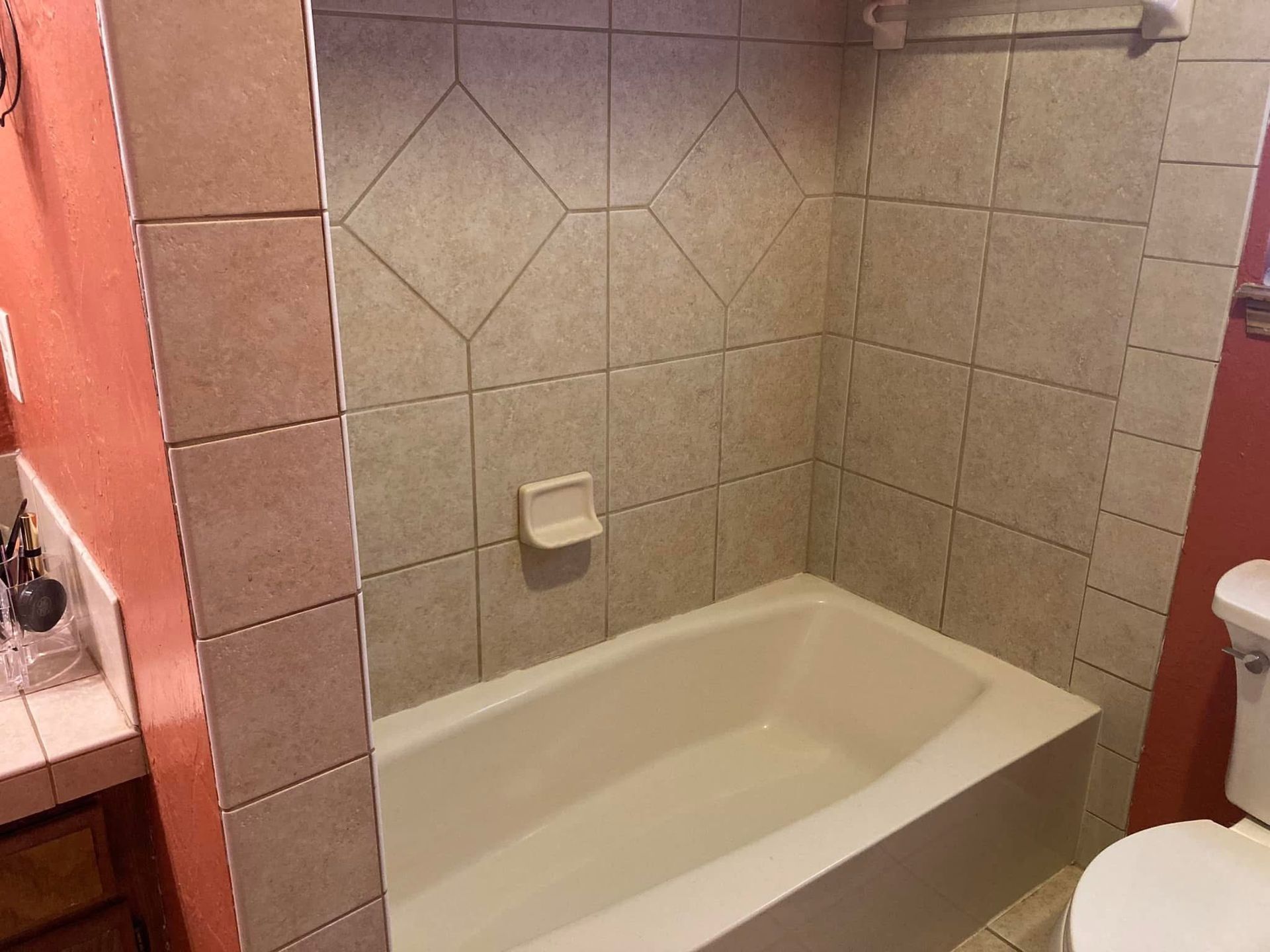 Bathroom with beige tiled walls around a white bathtub and a white soap dish. The walls are a peach color.