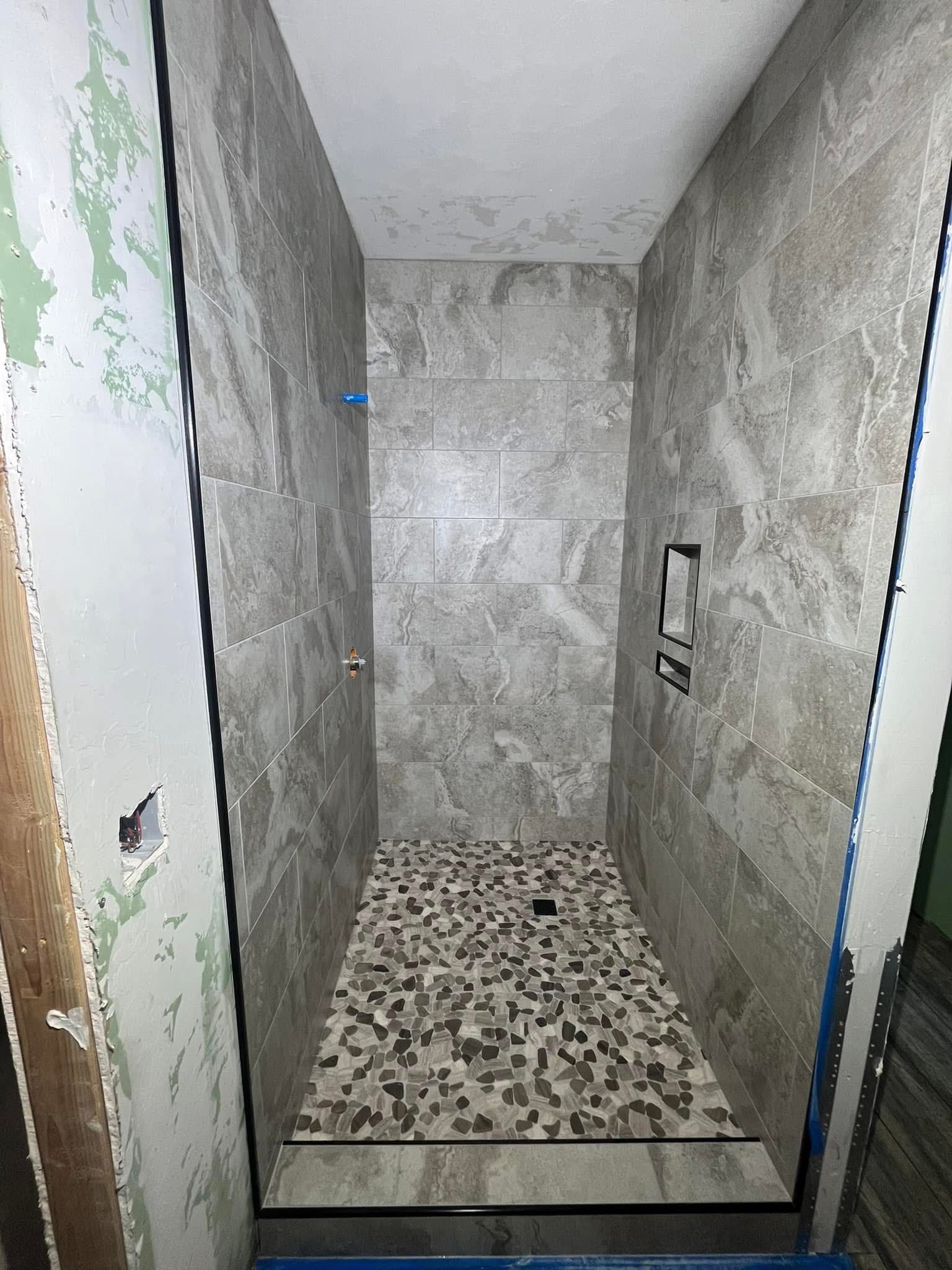 Narrow shower under construction with stone tile floor and walls, featuring a built-in niche, water fixtures, and a low curb.