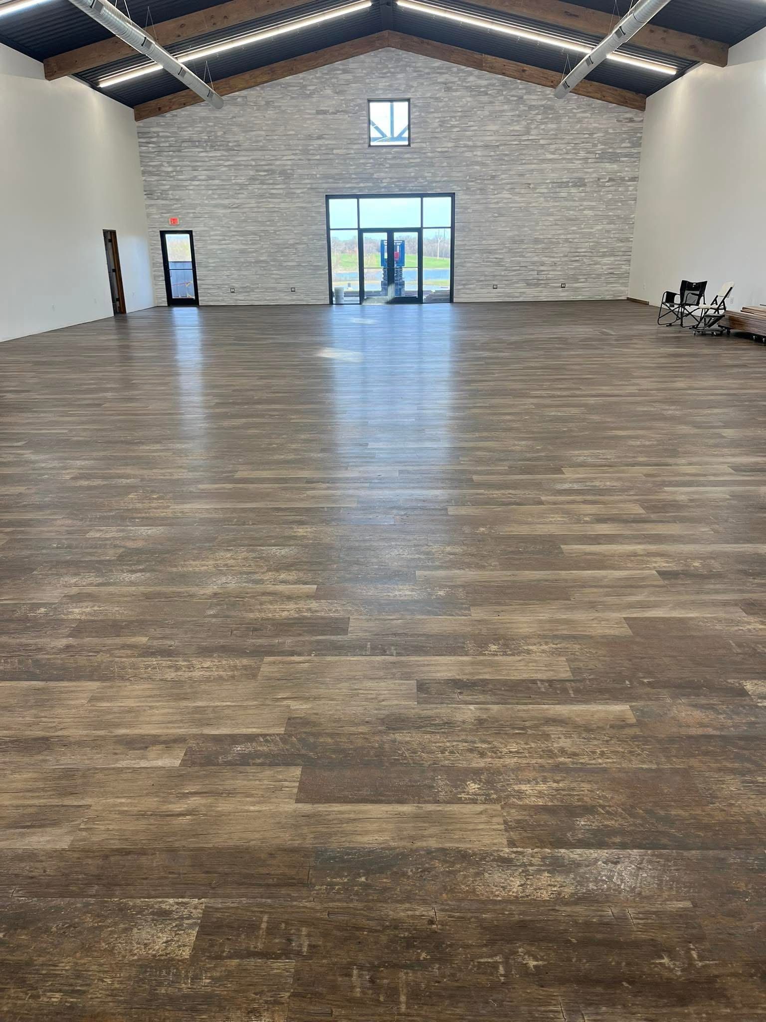 Interior of a large event space with wood-look flooring, a stone accent wall, and high ceilings.