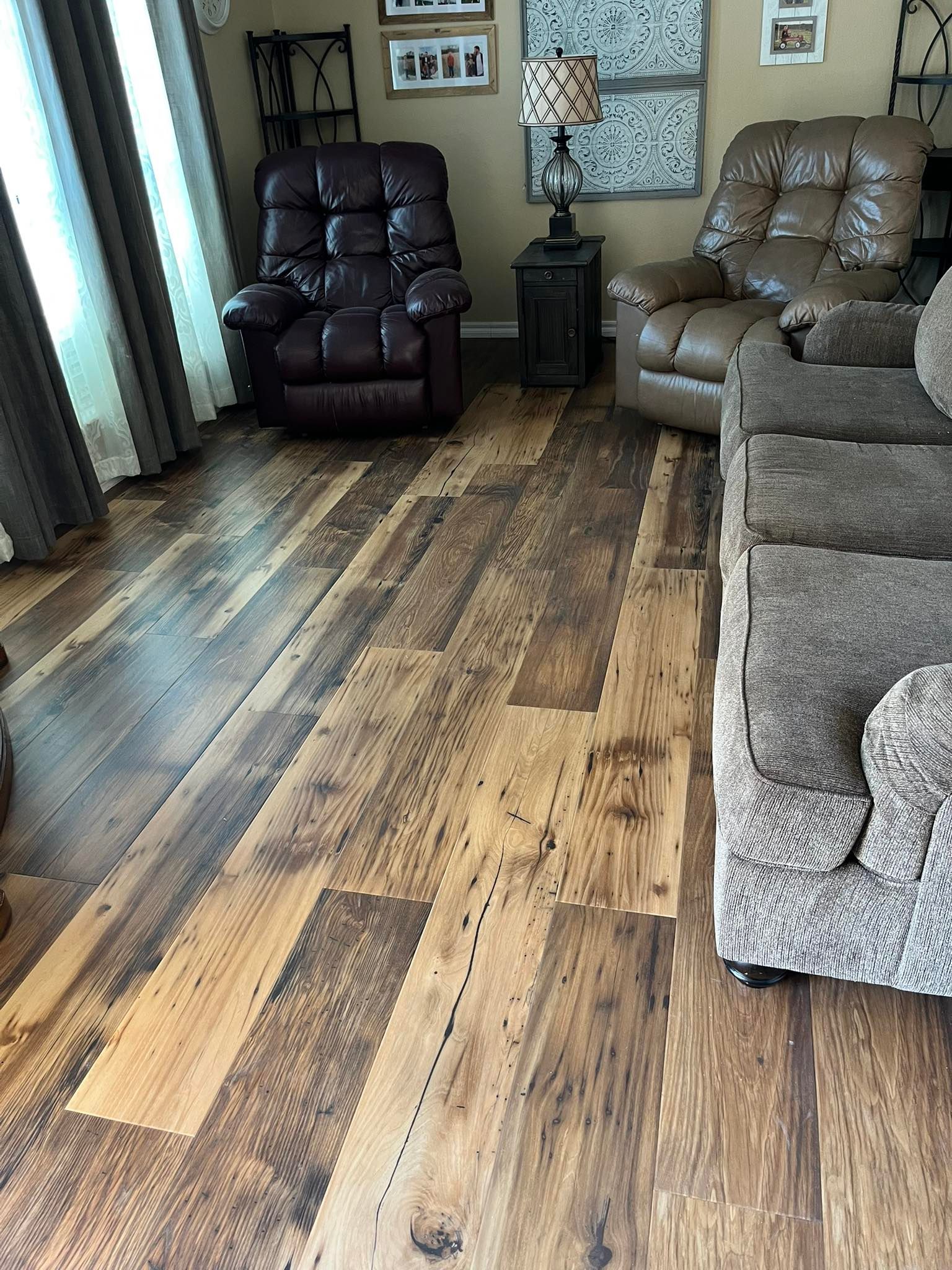 Living room with wood-look flooring, two recliners, and a sofa. The floorboards vary in shades of brown.