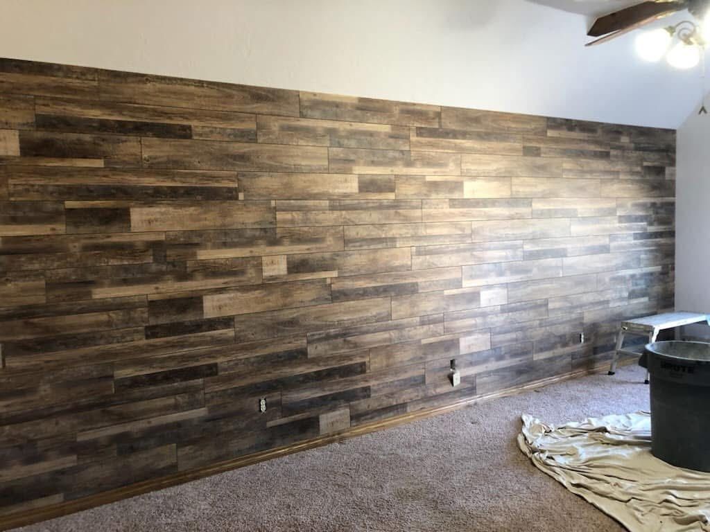 Wooden plank wall installed in a room, spanning the majority of the wall. The planks are various shades of brown and beige.