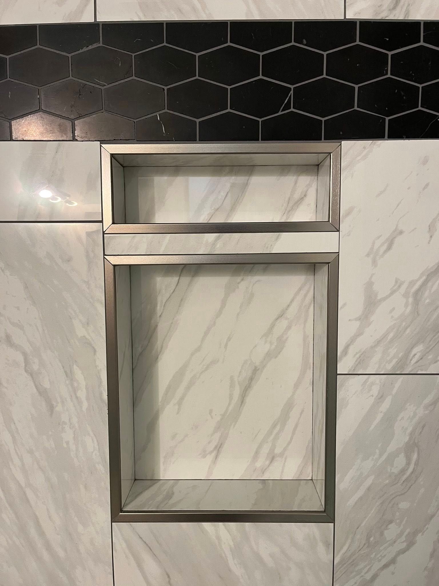 Shower niche with white marble-patterned tile, a stainless steel frame, and a black hexagon tile accent.